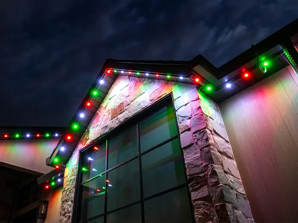 A building with exterior stone and wood siding decorated with colorful Christmas lights at night.
