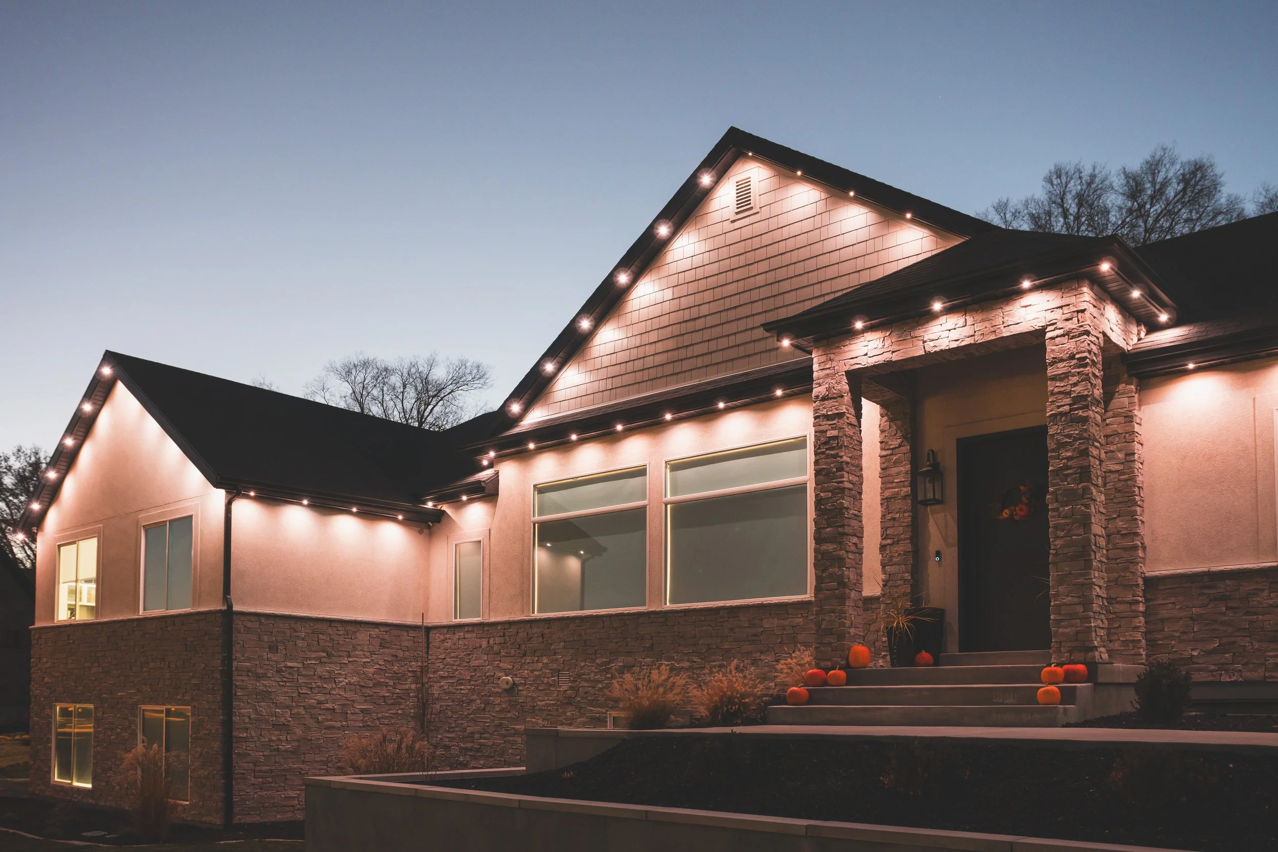 A modern house at dusk with eave lighting and pumpkin decorations on the steps.