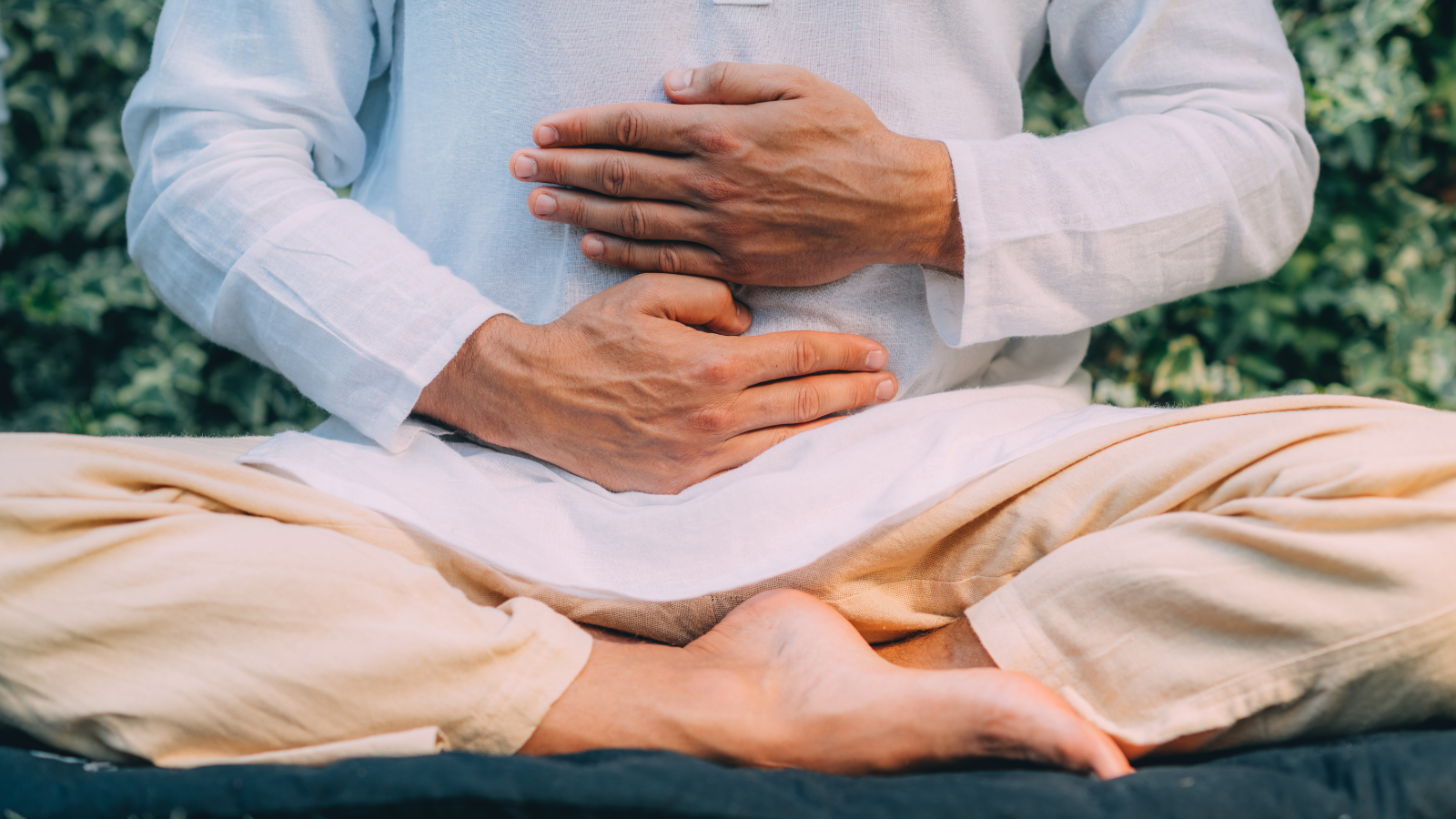 Person sitting cross-legged outdoors, practicing meditation with hands on stomach.