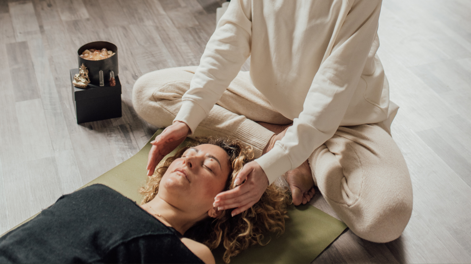 Person practicing Reiki or energy healing on a woman lying on a mat indoors.