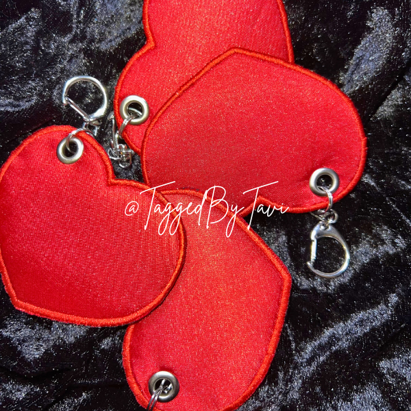 Red heart-shaped fabric keychain with metal hardware, resting on black velvet background.