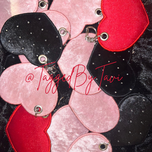A collection of pink, red, and black heart-shaped keychains with metal loops, some with small silver dots, displayed on a black surface.