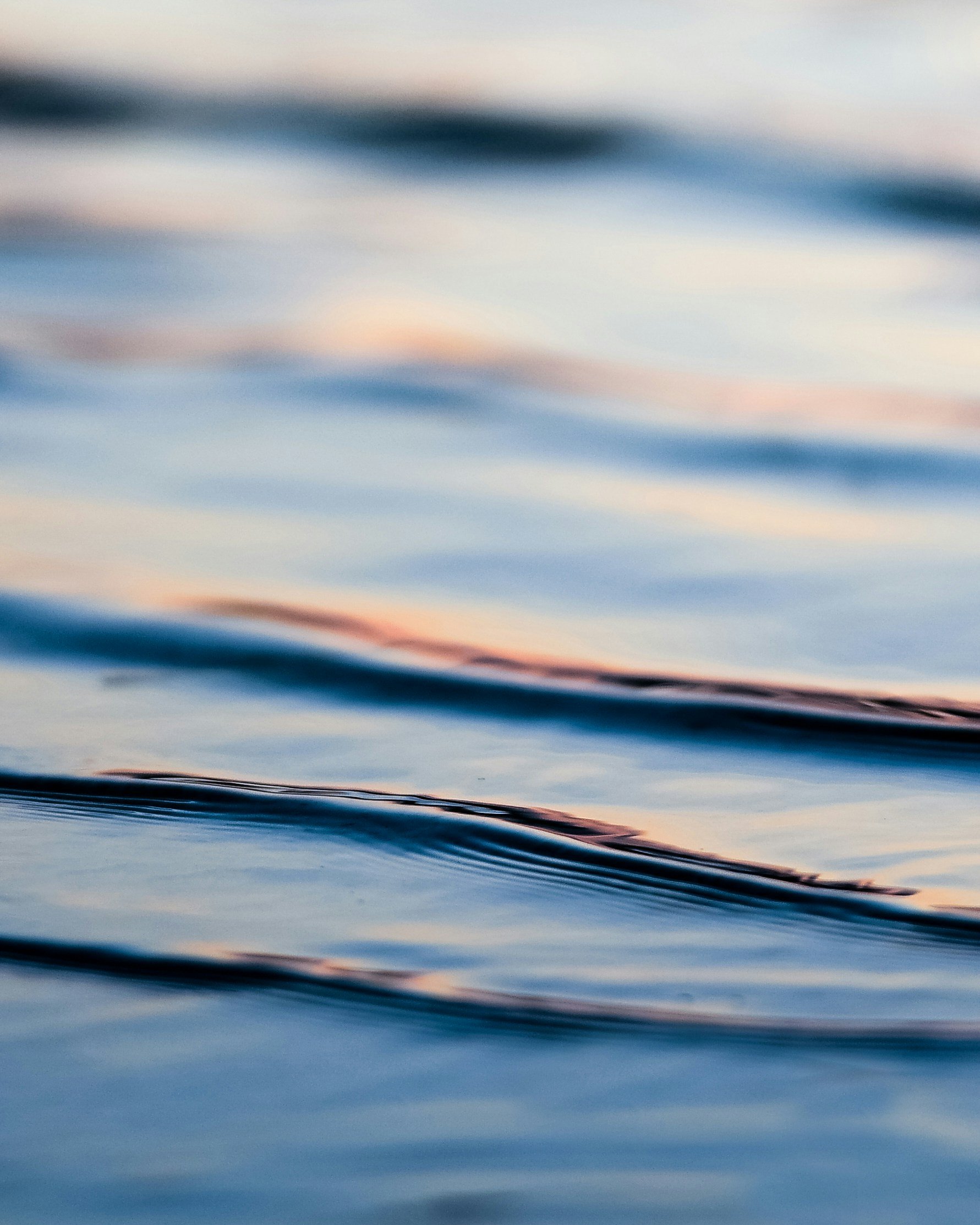 Blick auf die Wasseroberfläche bei Sonnenuntergang, mit sanften Wellen und reflektierenden Farben des Himmels.