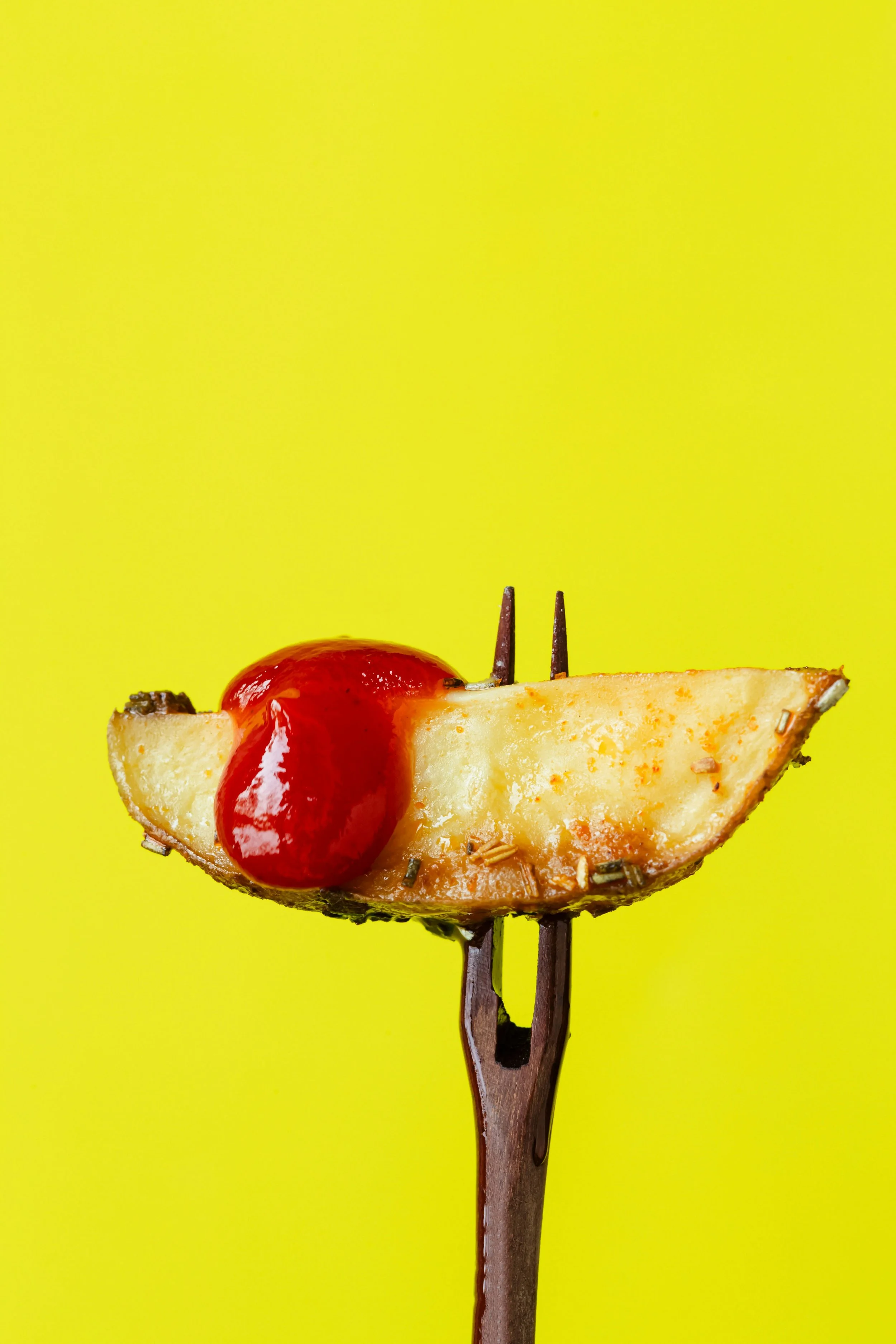 Single chunky chip with a drizzle of tomato sauce on a fork, on a bright yellow background