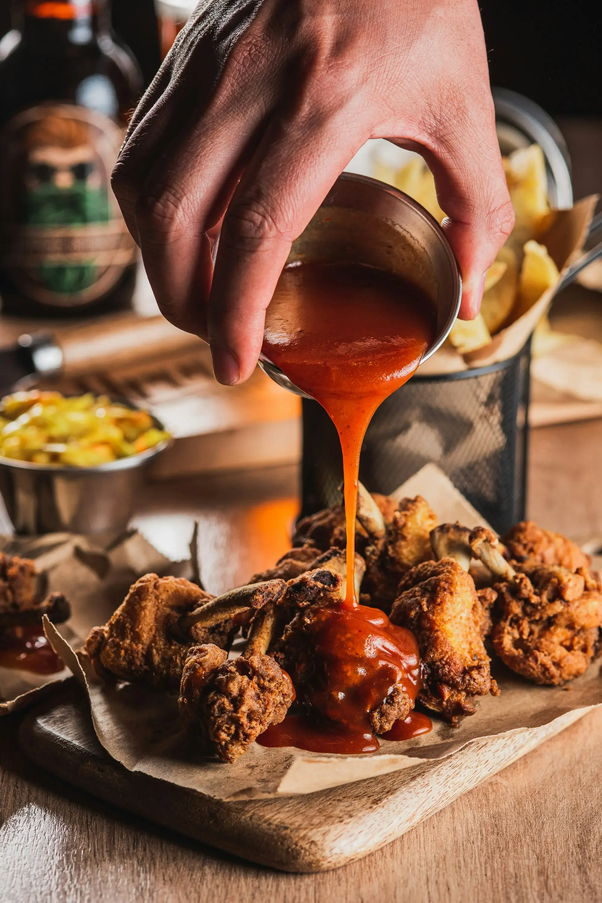 bbq sauce being poured onto a wooden tray of fried chicken