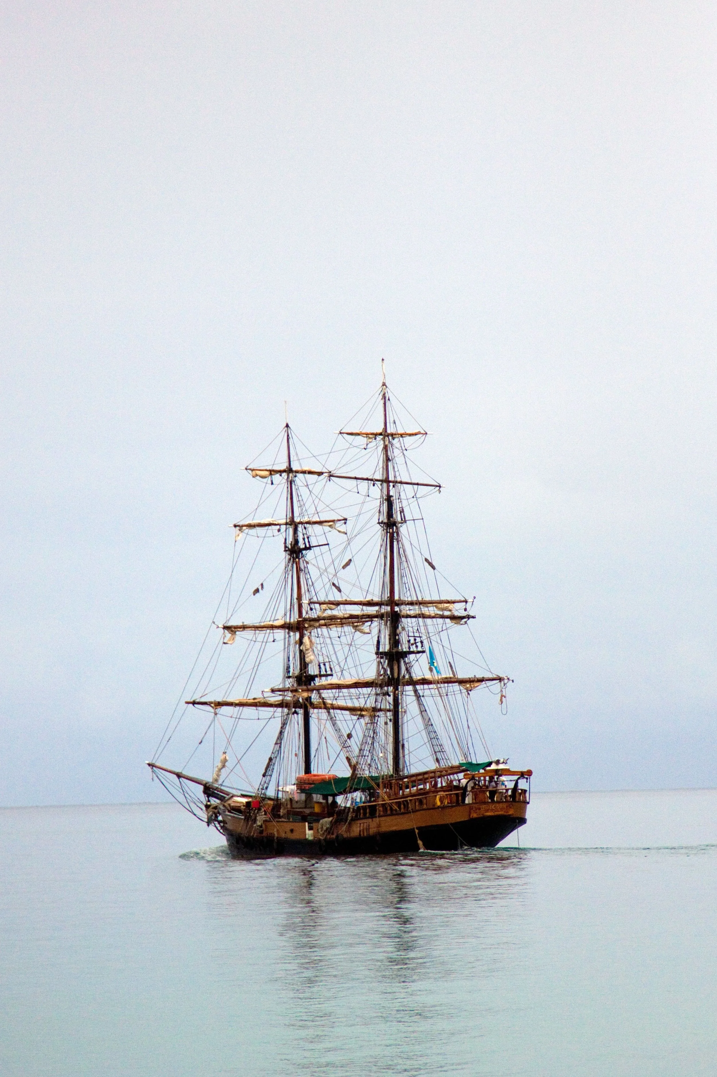A large wooden sailing ship with multiple masts and sails, floating on calm water under a cloudy sky.