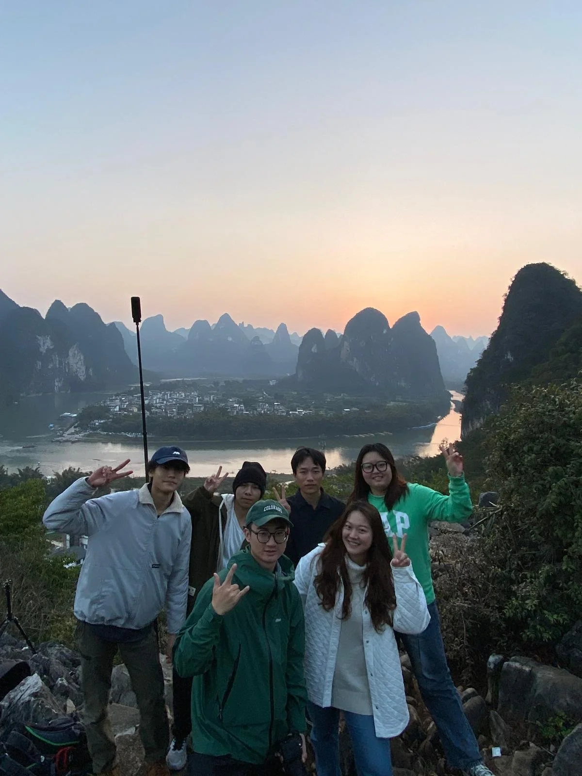 Group of six people posing outdoors with a river and karst mountains at sunset in the background.