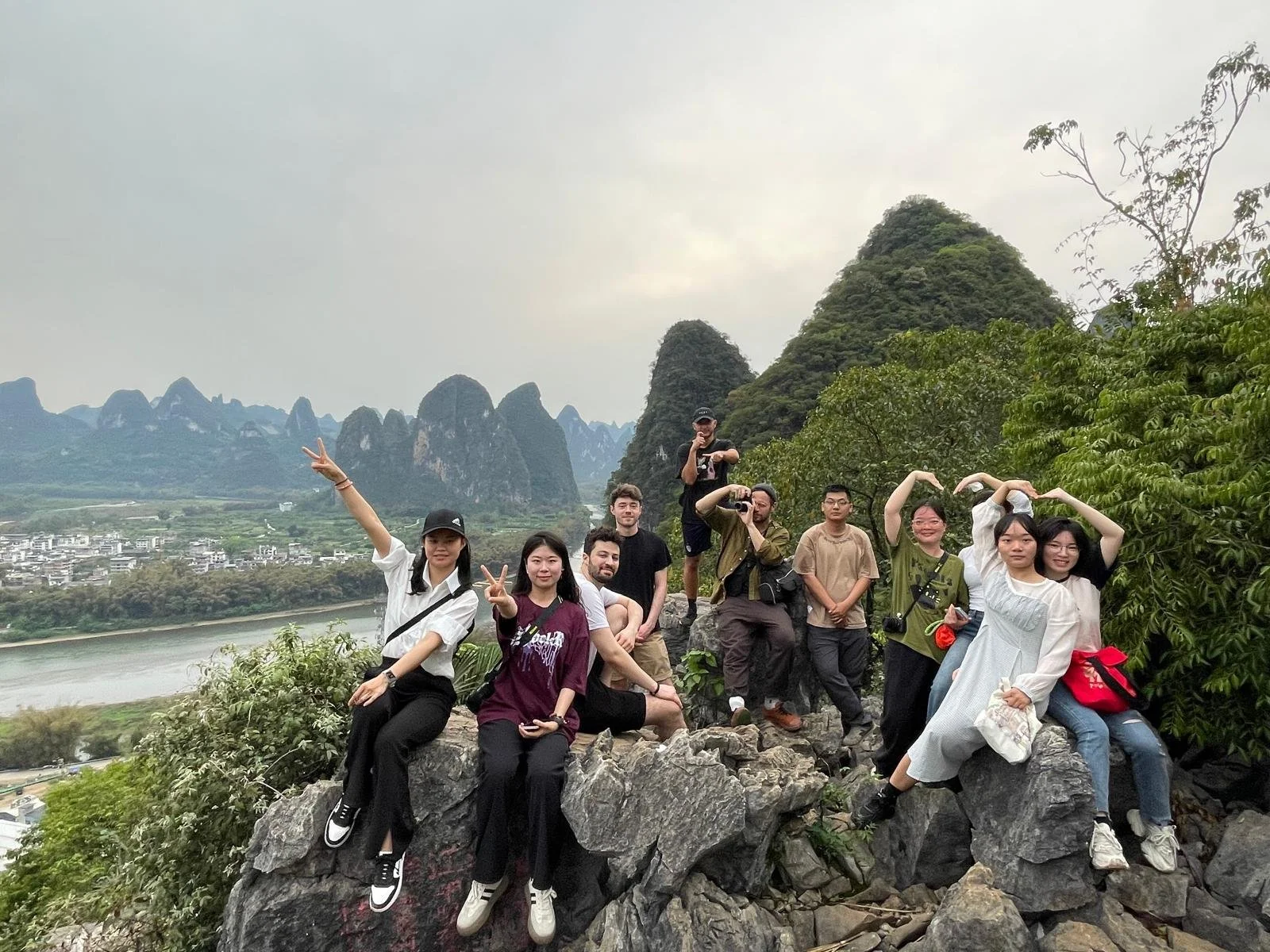 Group of people posing on rocks outdoors with mountains and river in the background.