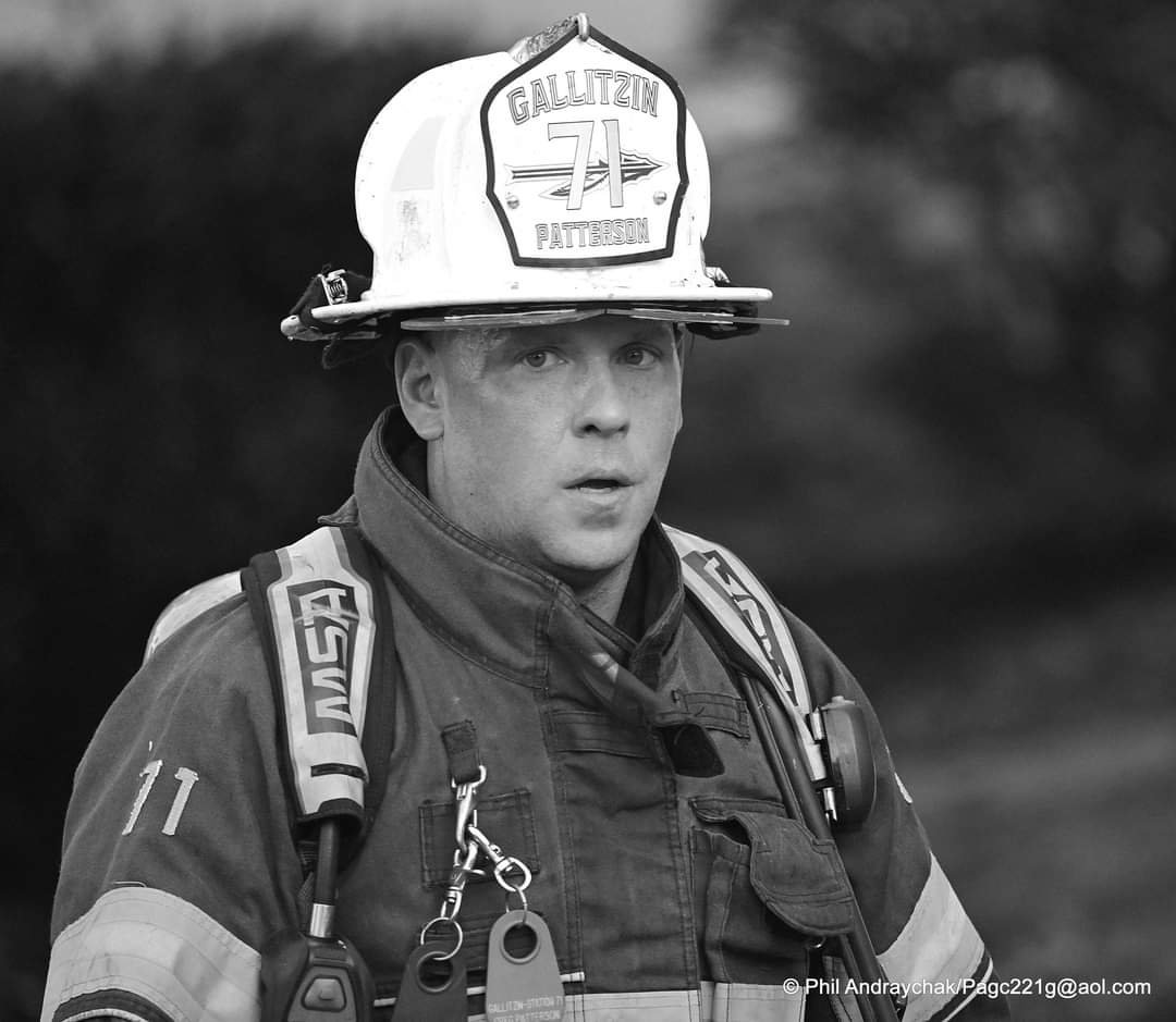 A firefighter wearing a helmet, uniform, and backpack, looking surprised or alert.