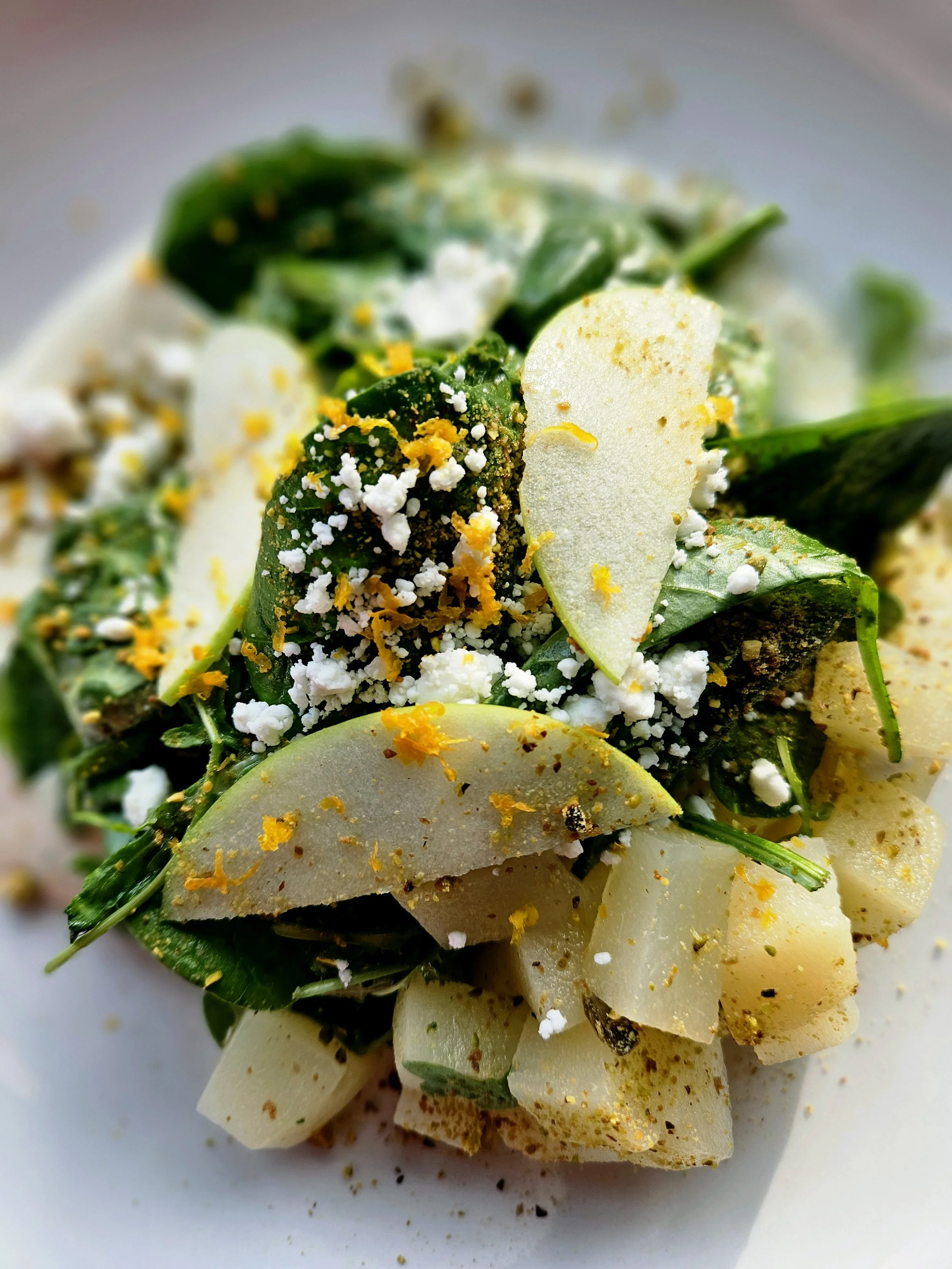 Close-up of a salad with sliced potatoes, greens, crumbled cheese, and sprinkled seasoning.