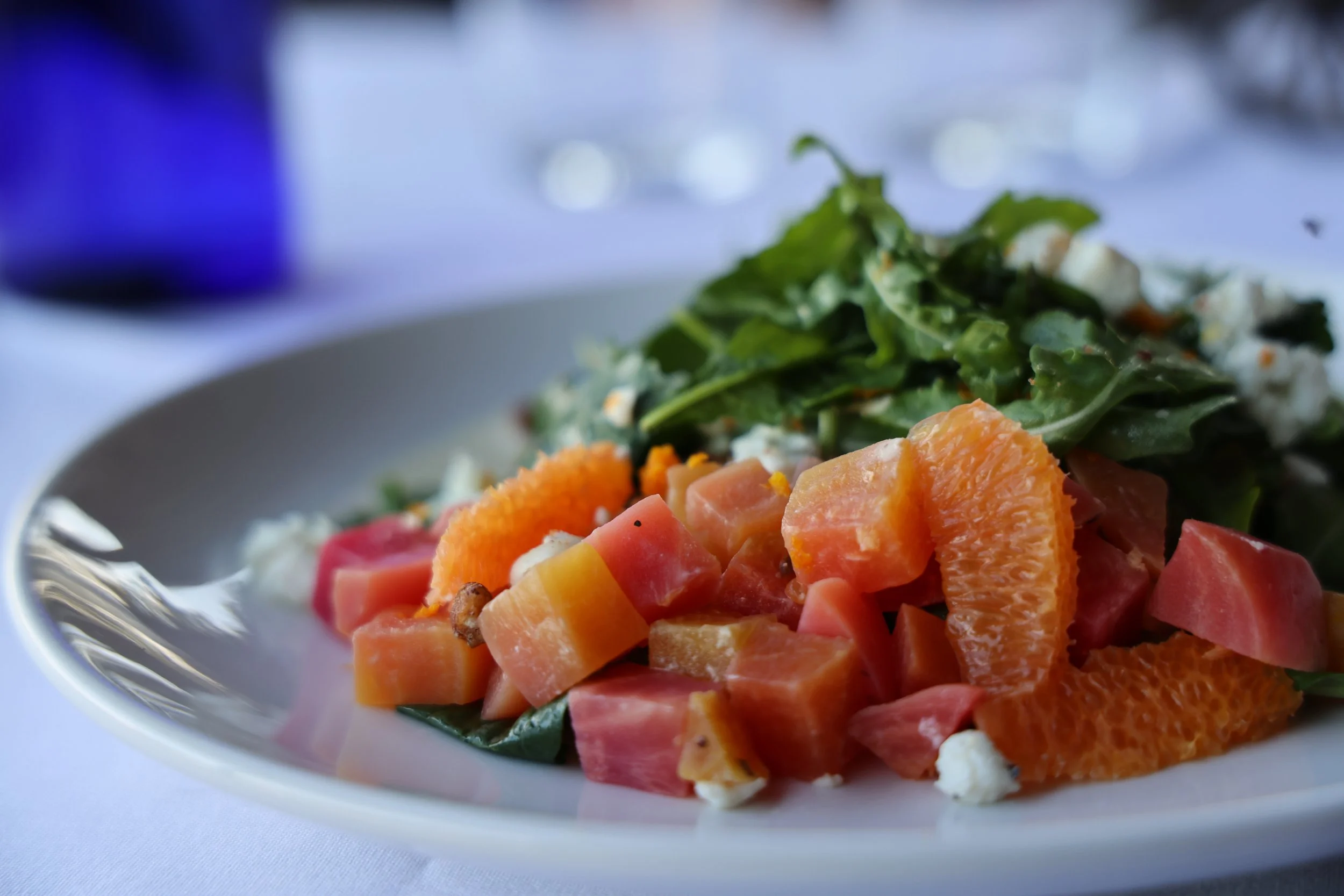 A plate of salad with mixed greens, orange slices, chopped fruit, and cheese on a white tablecloth.