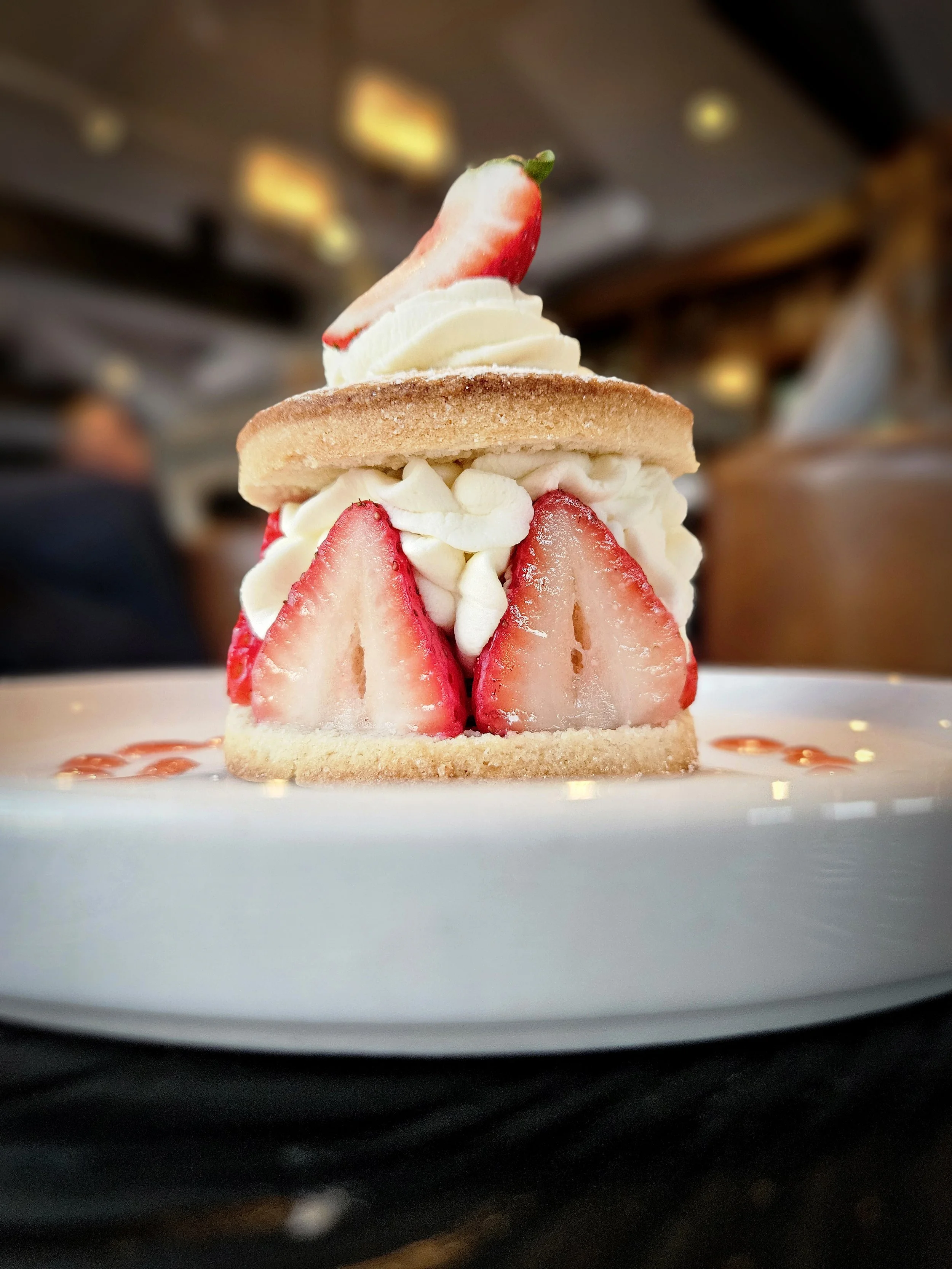 Strawberry shortcake with sliced strawberries, whipped cream, and a cookie, served on a white plate.