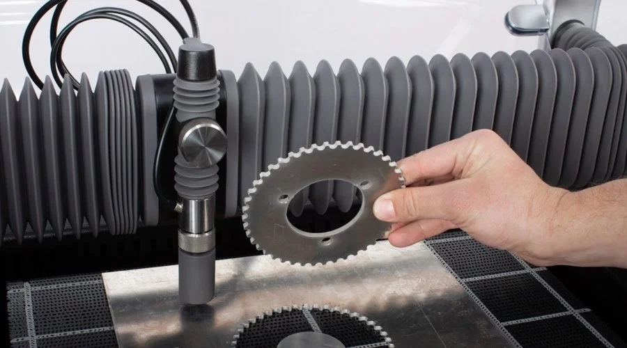 A person holding metal gasket in front of a large industrial water jet machine with flexible hoses.