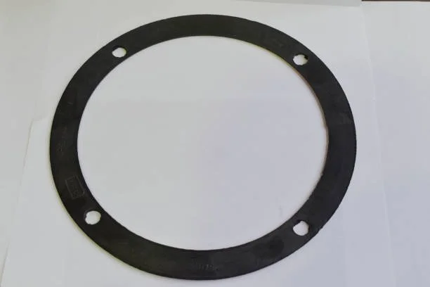 A black rubber or plastic gasket with four holes, placed on a white surface.