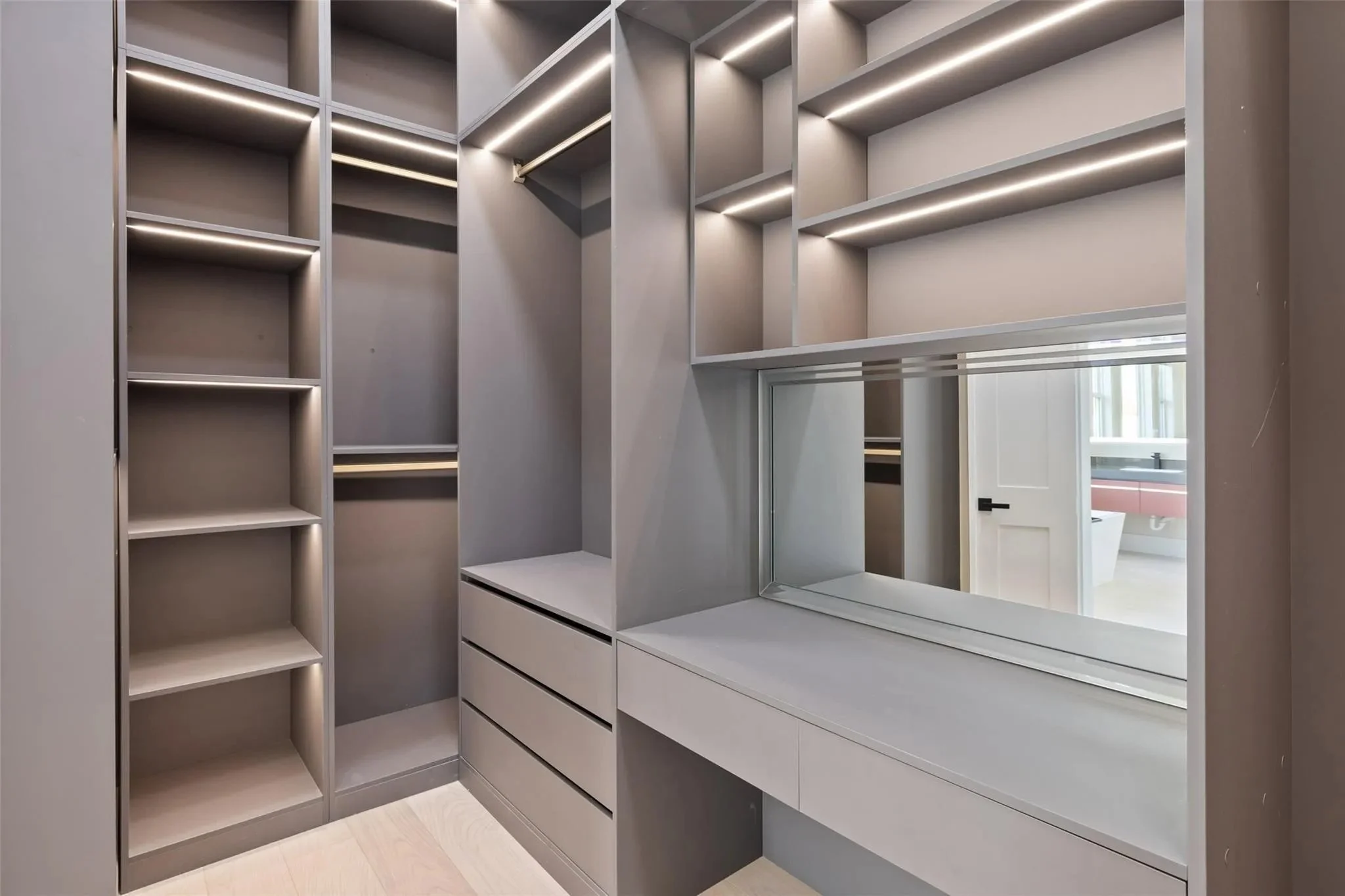 A modern walk-in closet with custom gray cabinetry, open shelves, drawers, and a mirror.