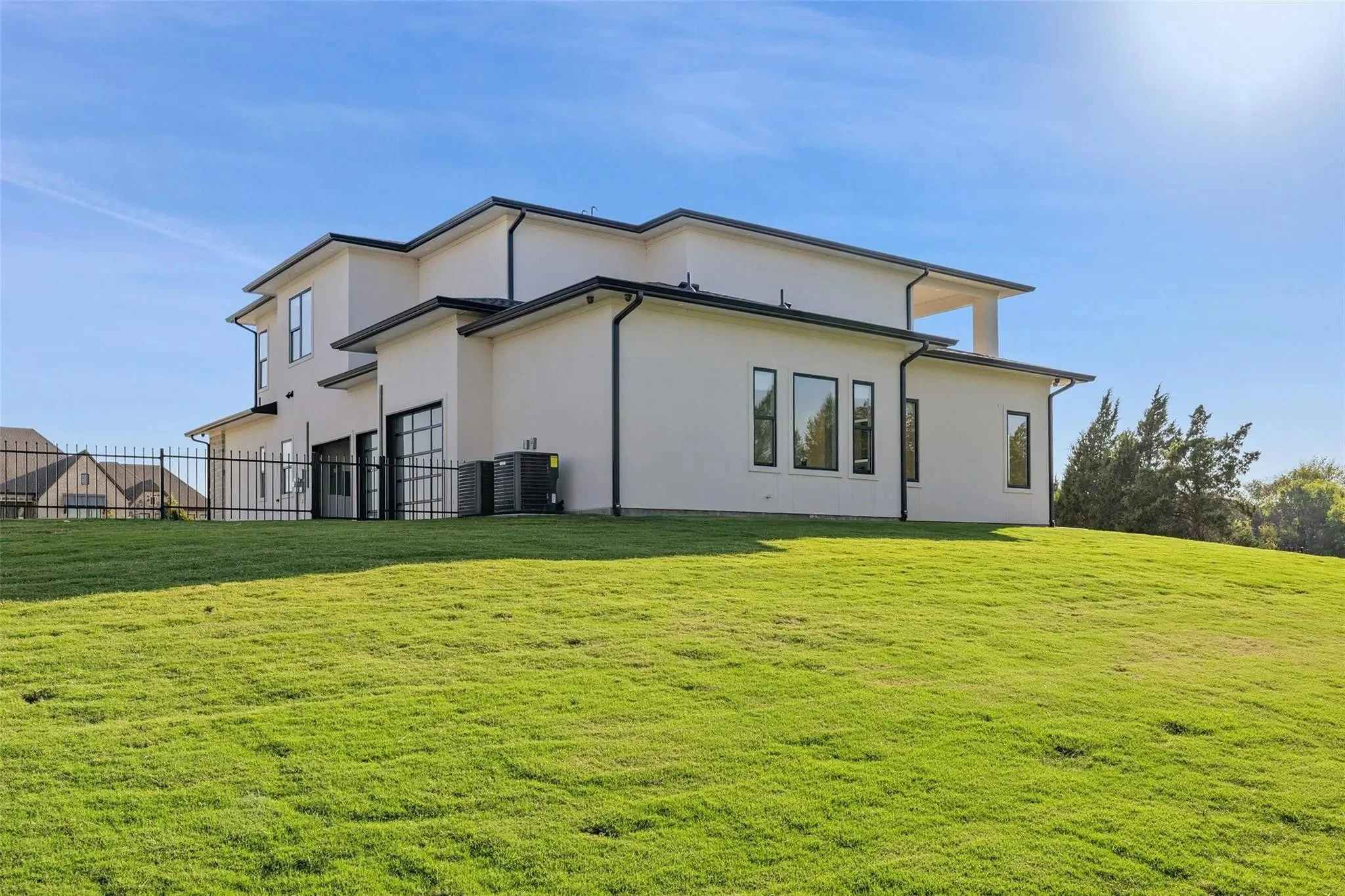 Modern white two-story house with multiple windows situated on a grassy hill under a blue sky.