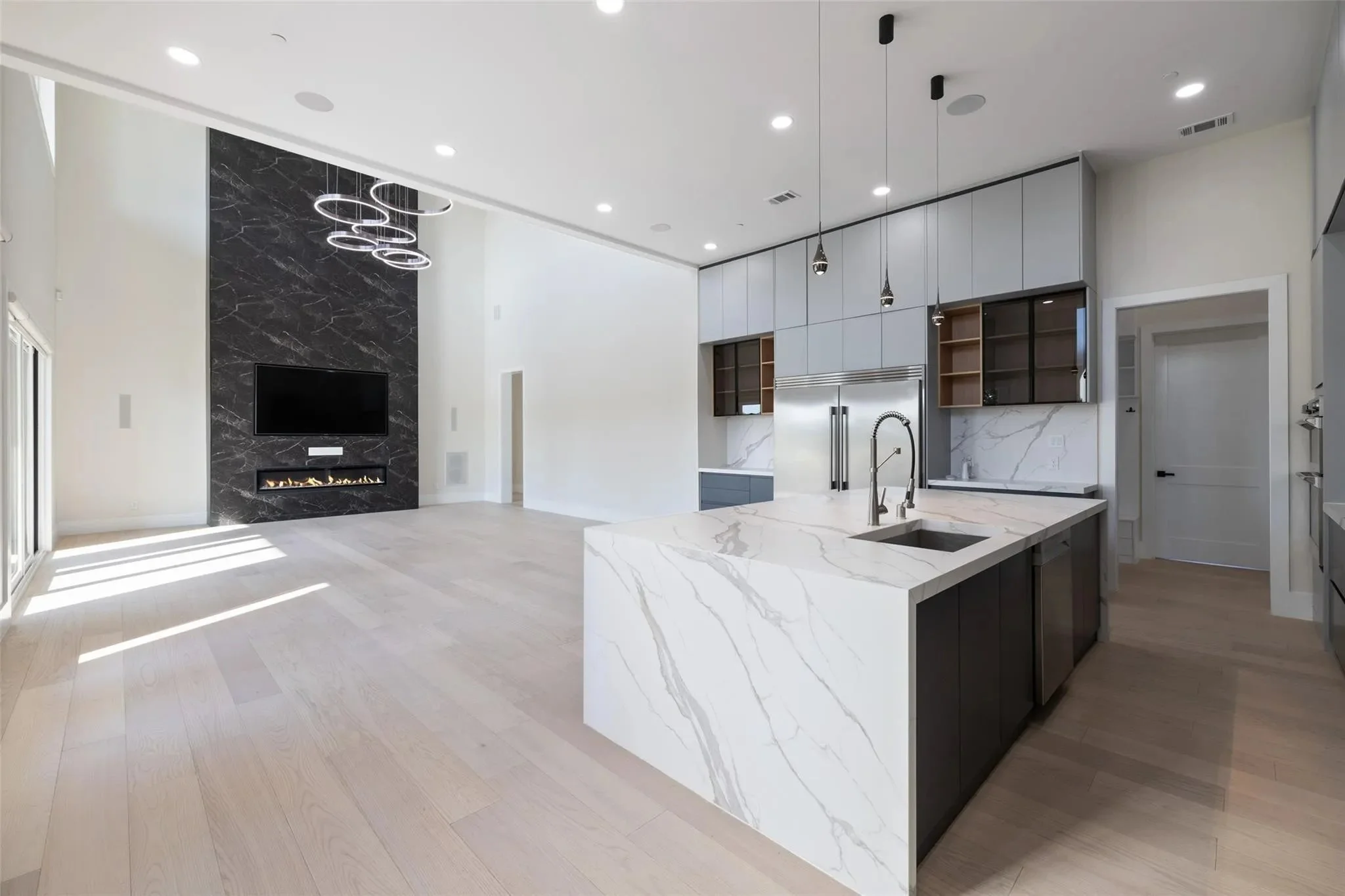 Modern open-concept kitchen and living room with white marble island, gray cabinetry, and a black accent wall with a mounted TV and fireplace.