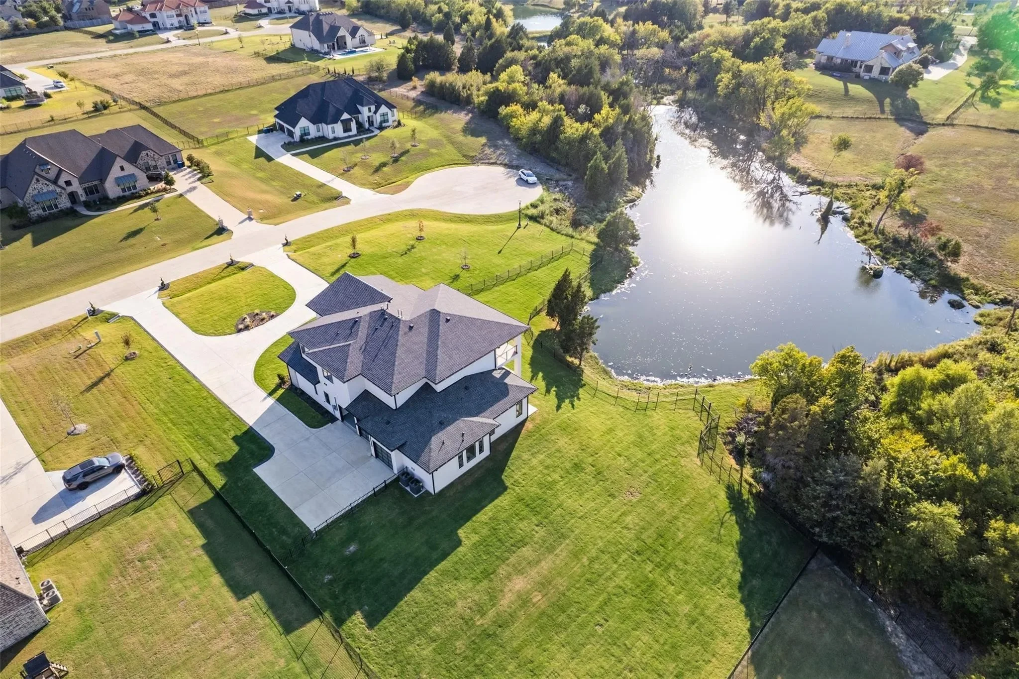 Aerial view of a residential neighborhood with a large house near a pond, surrounded by well-maintained lawns and trees.