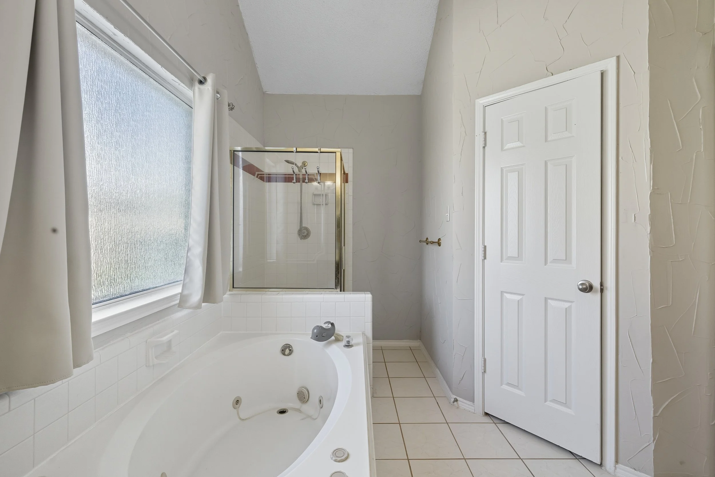 Bathroom with a bathtub, a frosted window, a glass-enclosed shower, and a closed white door.