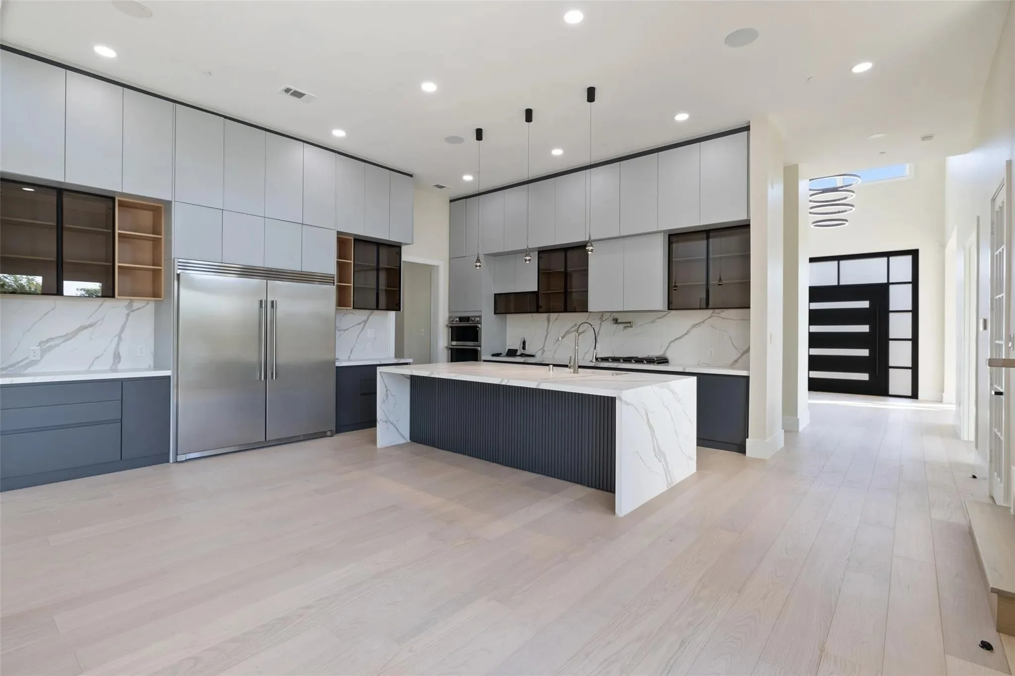 Modern kitchen with white marble island, gray and wood cabinetry, stainless steel appliances, and light wood flooring.