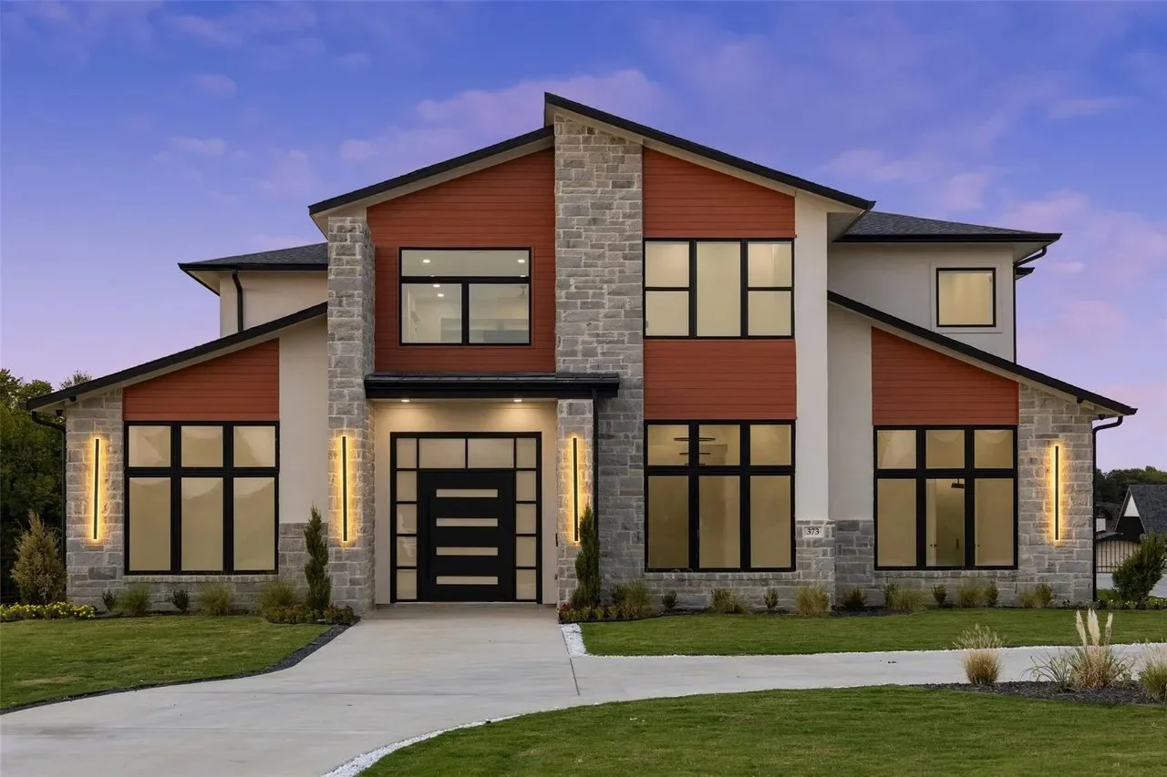 Modern two-story house with stone and wood exterior, large windows, front yard, and driveway.