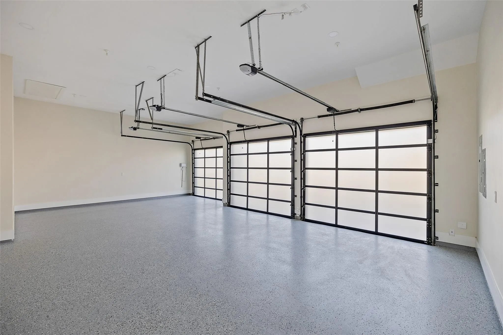 Empty garage with three closed sectional doors, ceiling-mounted garage door openers, and tracking systems
