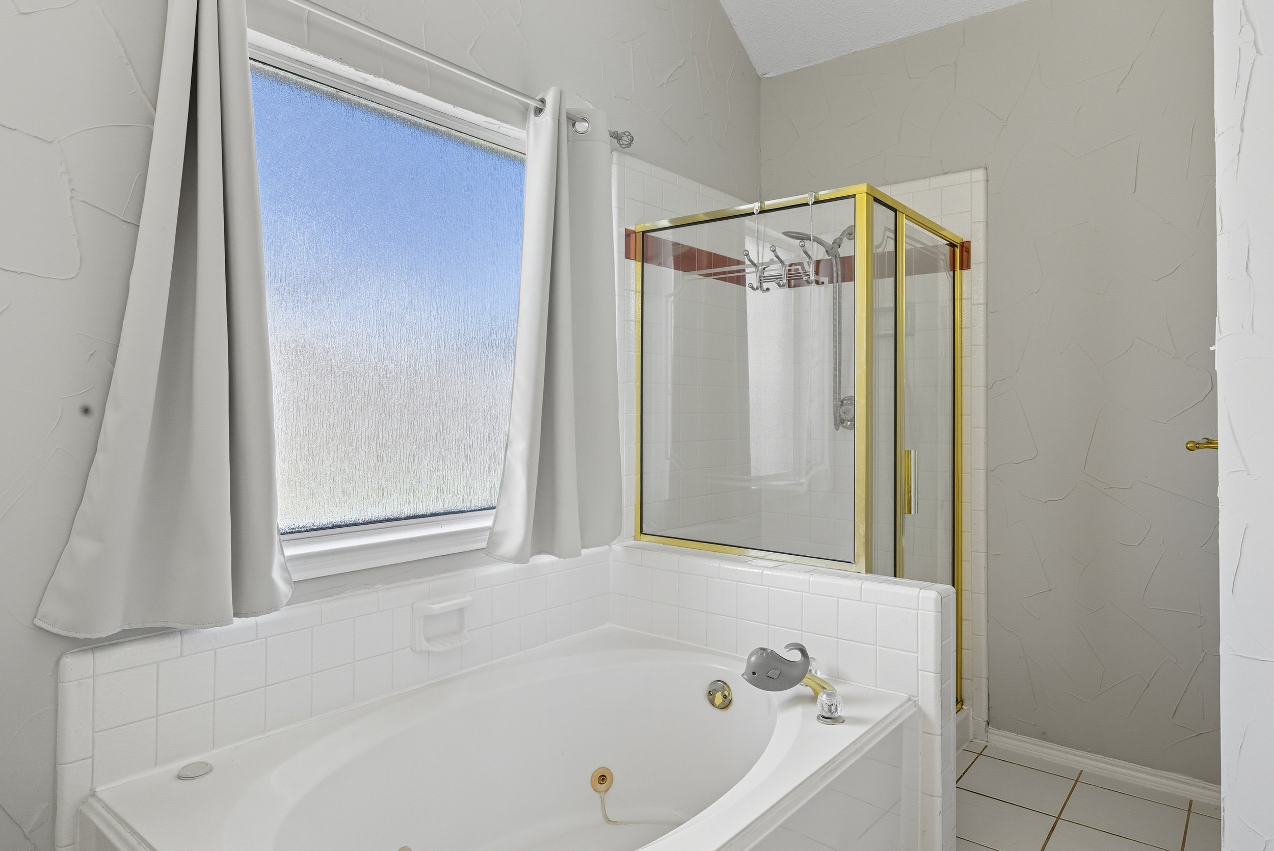 Bathroom with a large bathtub, frosted window, and a glass shower enclosure with gold trim.