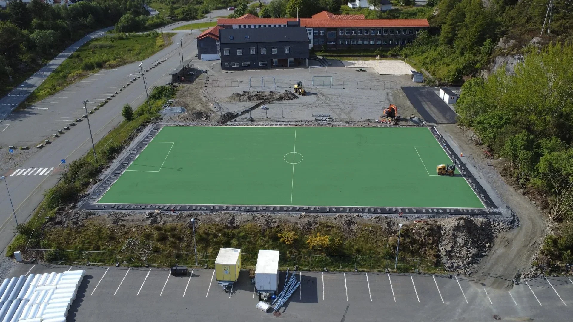 En fotballbane under bygging, med gravearbeid rundt og en illustrasjon av den ferdige gressmatten