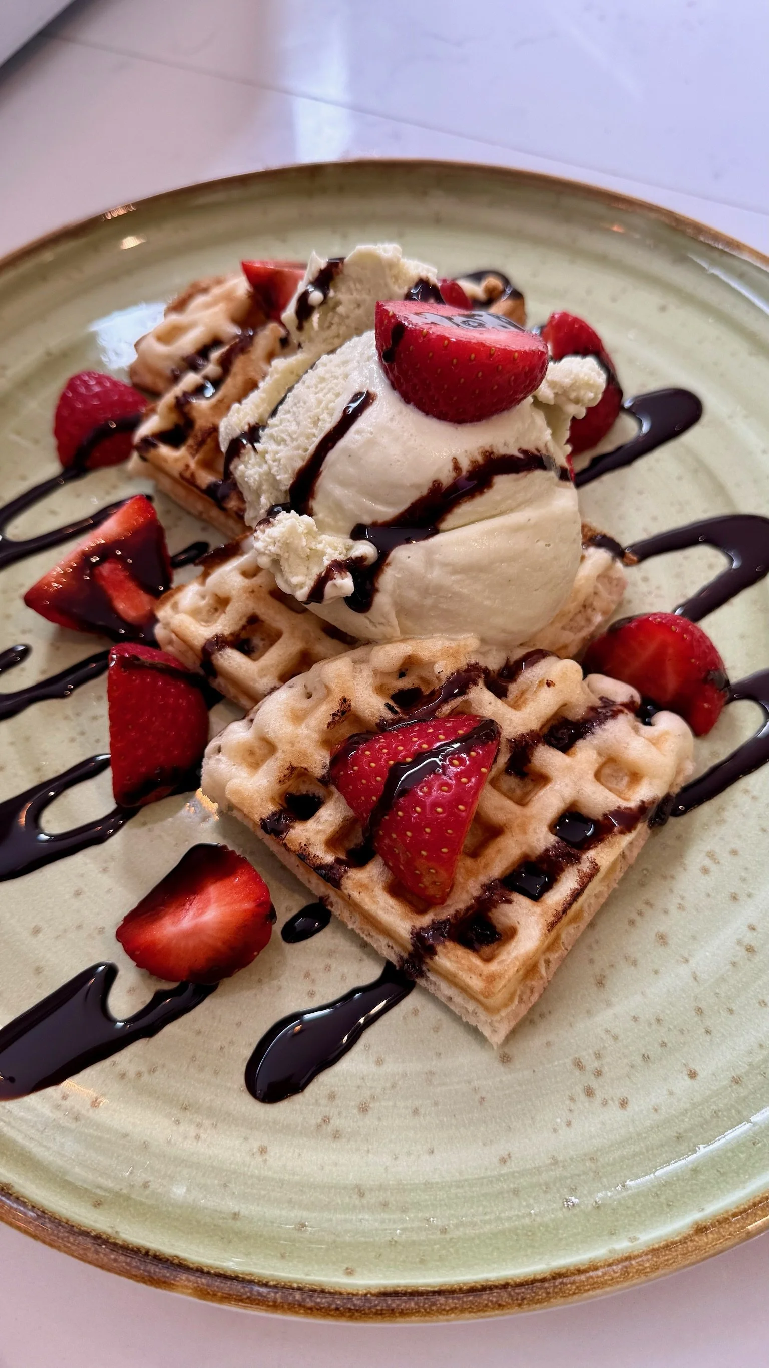 A plate of waffles topped with strawberries, a dollop of whipped cream, and drizzled with chocolate sauce.