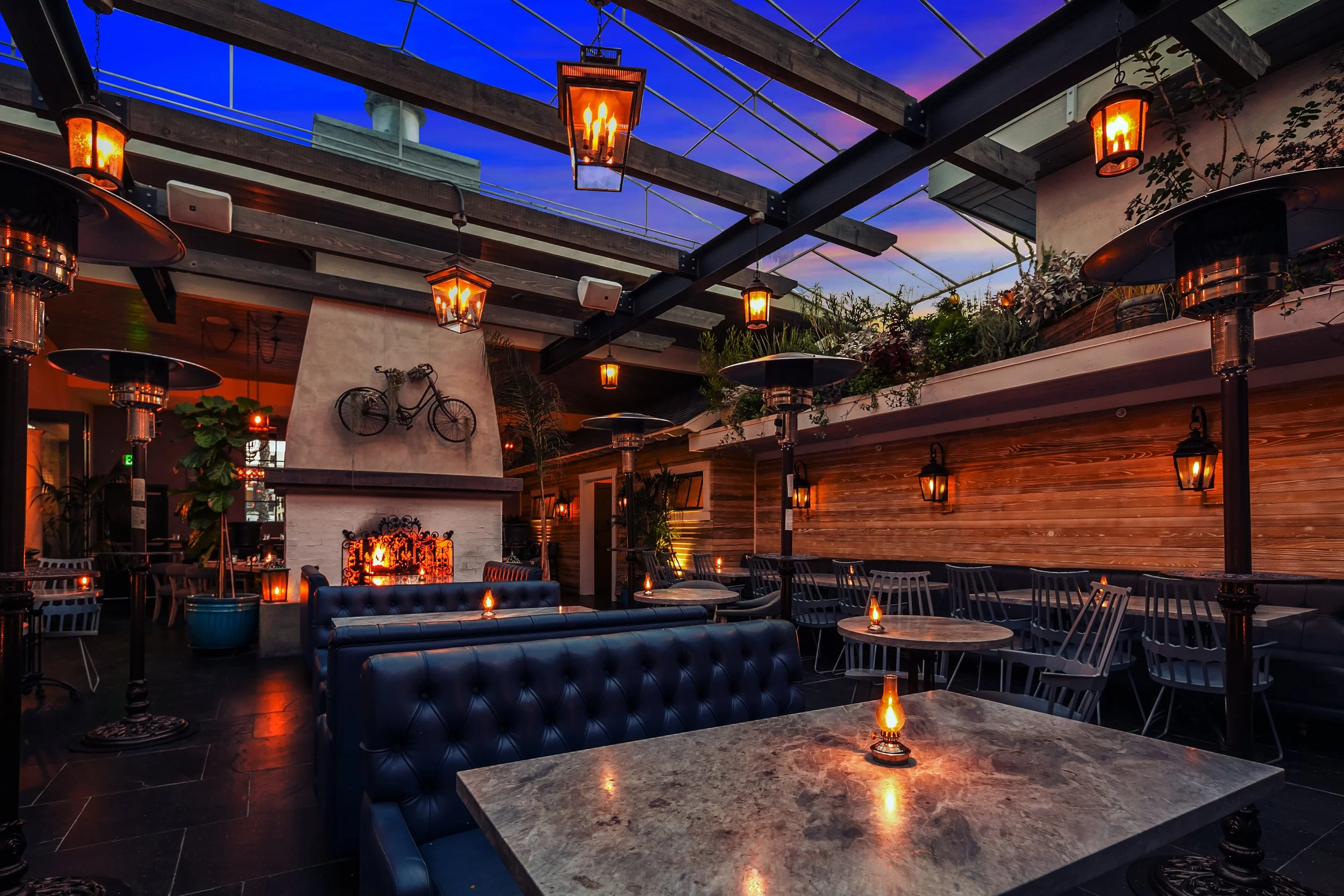 Herb & Wood dining room in Little Italy San Diego, with a fireplace, tufted leather booths, pergola, and lanterns at sunset — available for private events near San Diego