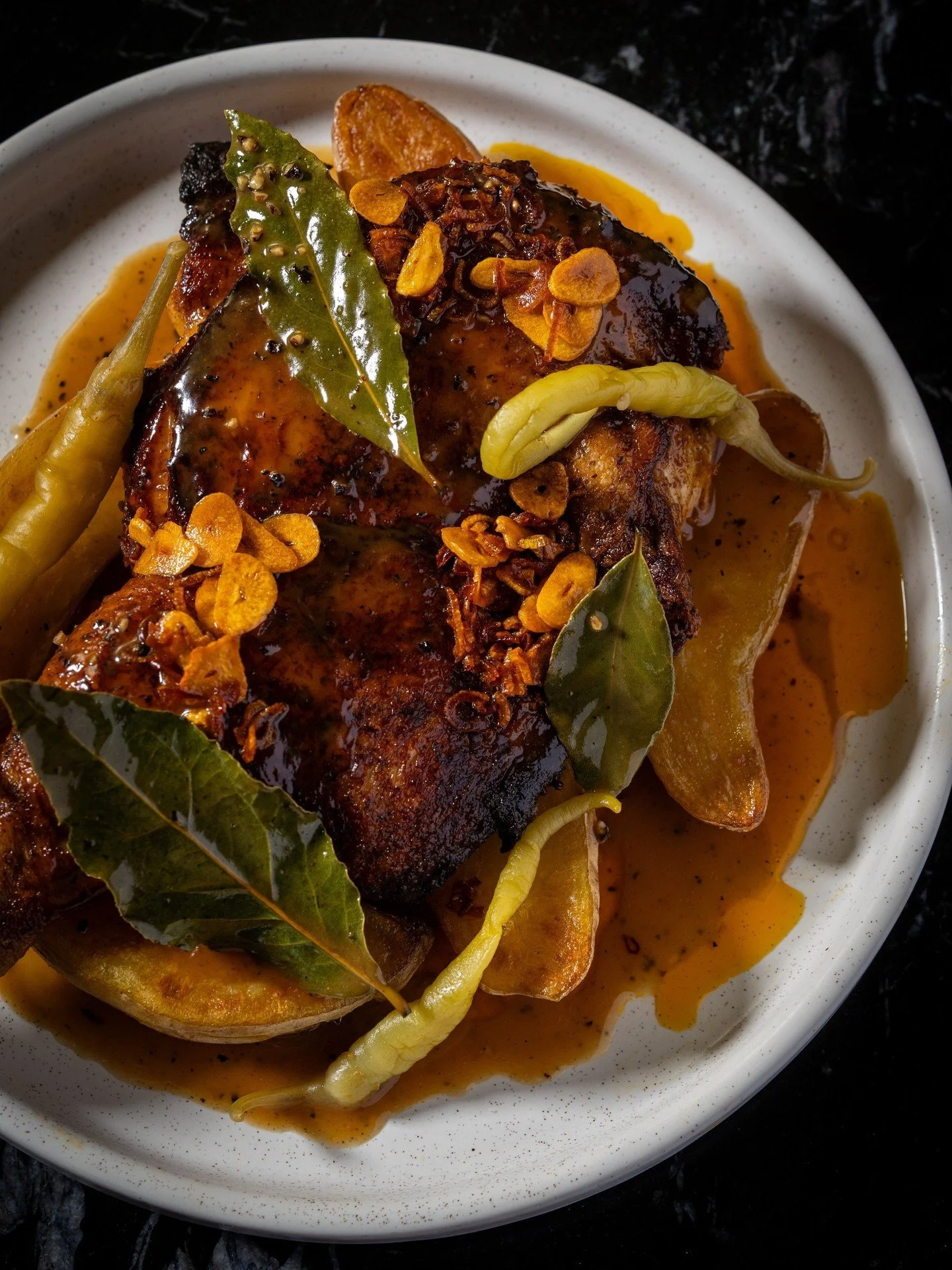 You probably know soy-based adobo, but our Chicken Adobong Pula, a red adobo, skips the soy and goes with fish sauce for a deeper hit of umami. Annatto, crispy garlic-shallot oil, yu choy, and piparra peppers round it out.
