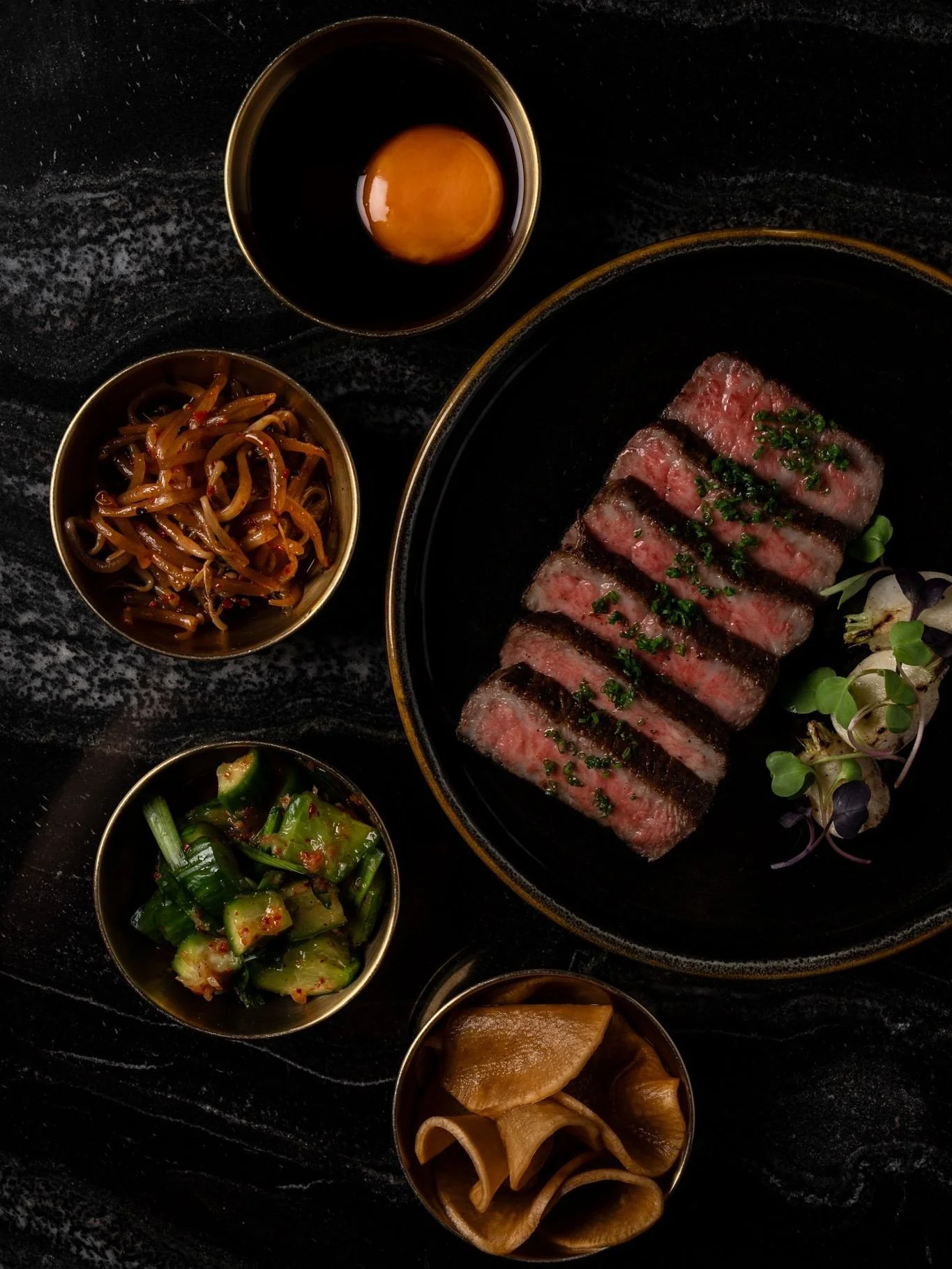 A5 Wagyu with the right company. Served with an assortment of banchan including pickled cucumber, sesame sprouts, kimchi, and egg yolk nikiri shoyu.