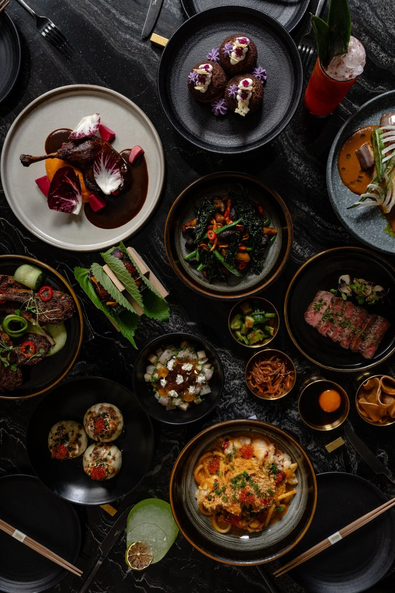 A spread of Asian-fusion dishes at Animae San Diego, including sliced wagyu, braised duck, stir-fried greens, tuna crudo, and various small plates.
