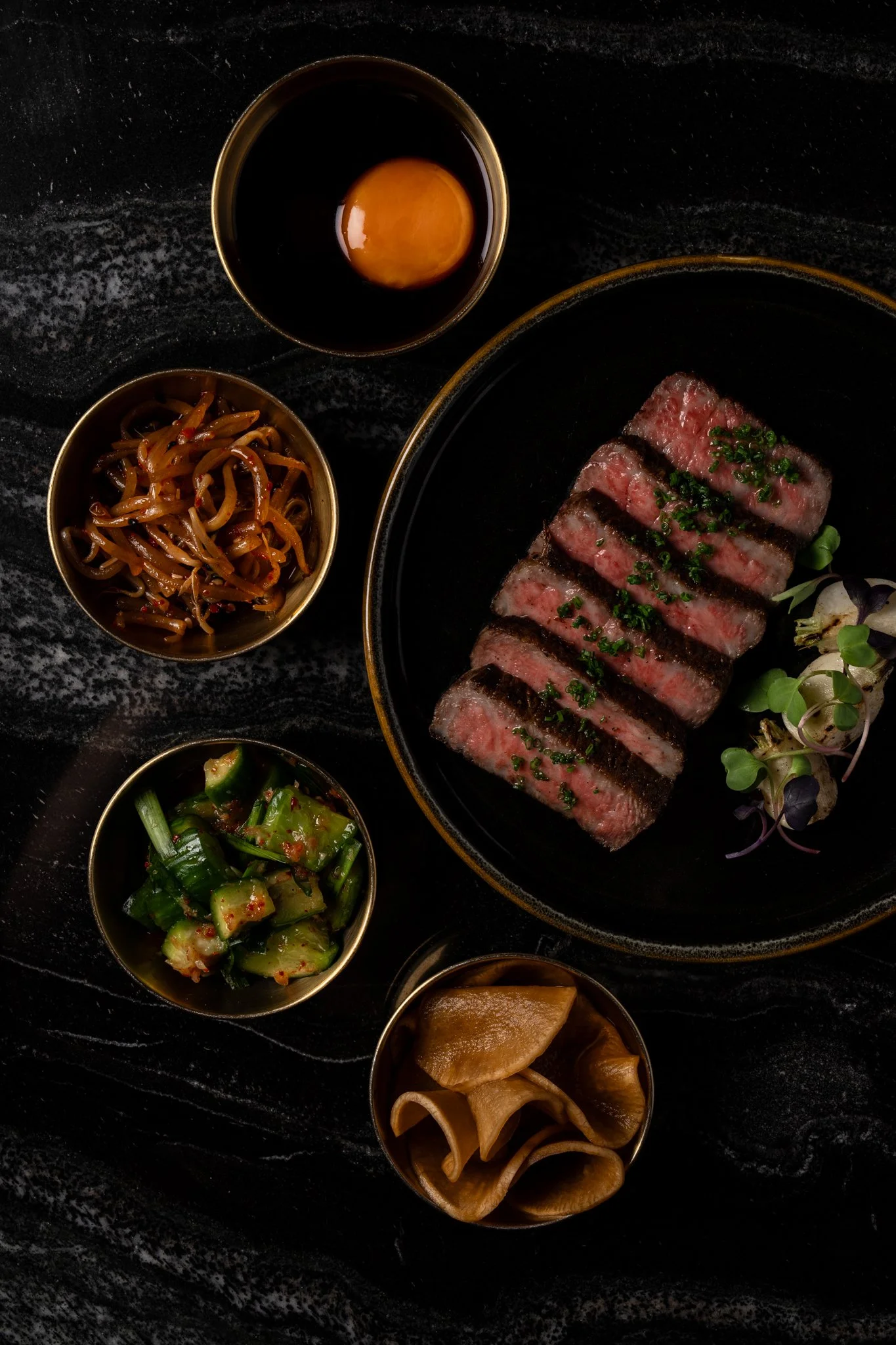 Sliced Japanese A5 wagyu served alongside small bowls of pickled radish, cucumbers, and soy sauce with an egg at Animae San Diego