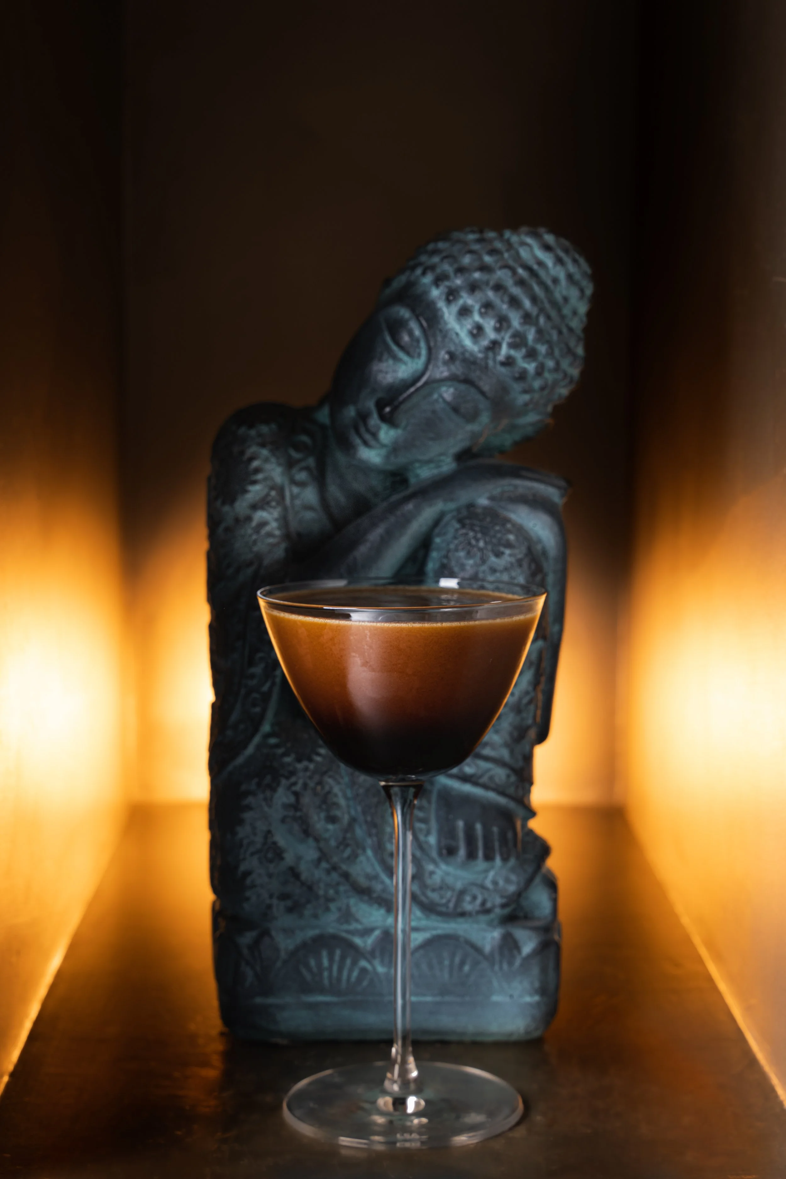 A dark espresso martini in a coupe glass with a Buddha statue and warm candlelight at Animae San Diego
