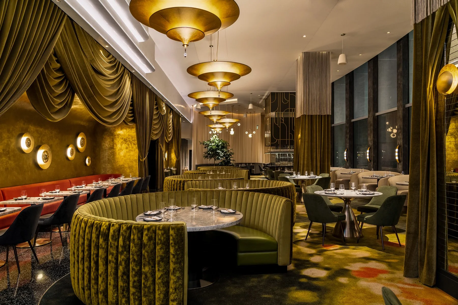 Full dining room at Animae San Diego, featuring olive velvet curved booths, stacked gold pendant lights, draped walls, and Art Deco design