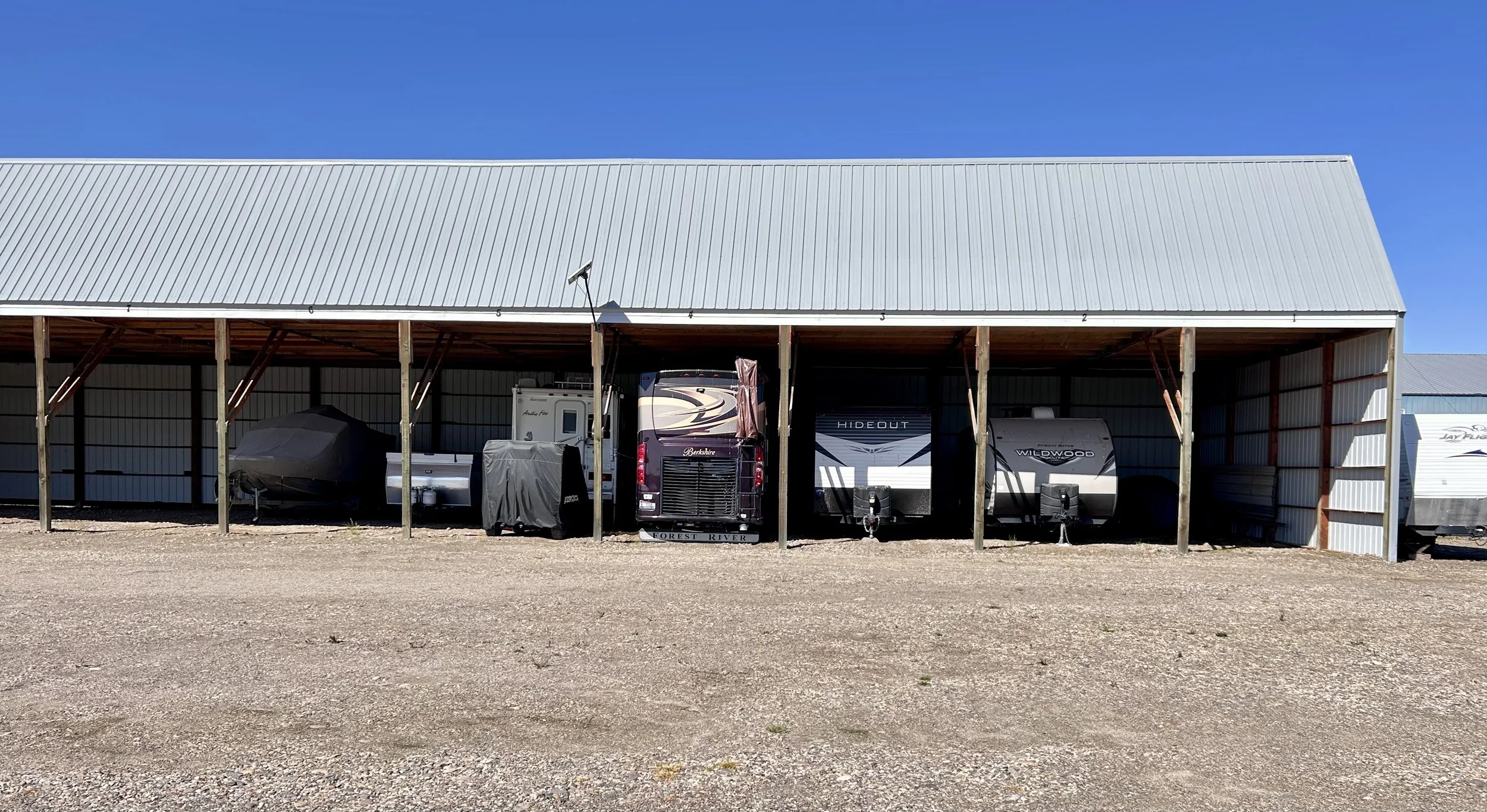 Outdoor storage shed with RVs, camper trailers, and boats inside.