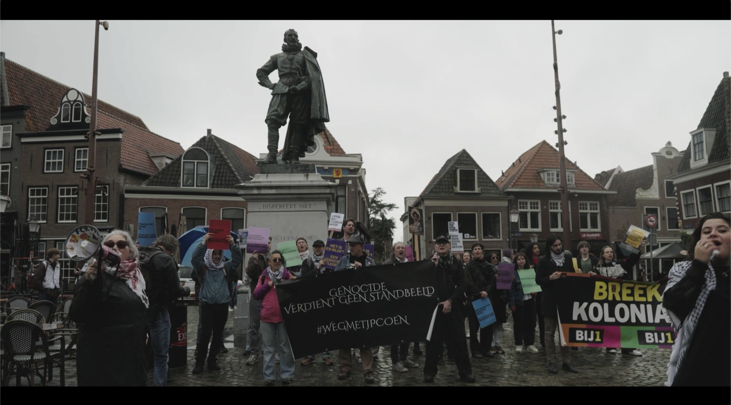 Protesterende menigten die banners vasthouden, voor een standbeeld in een stad met historische gebouwen op de achtergrond.