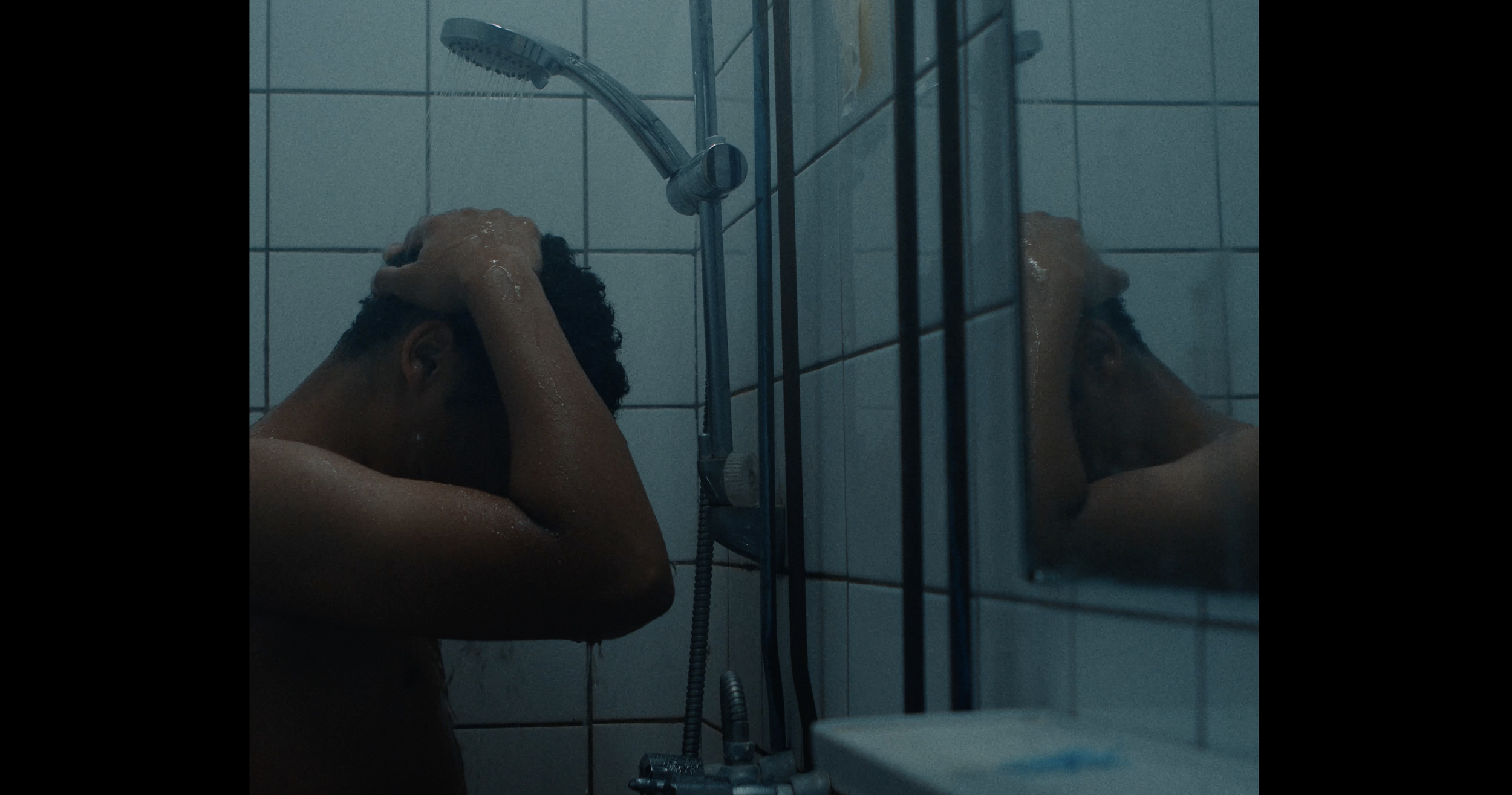 Man onder de douche, zijn hoofd in zijn handen, spiegel reflectie zichtbaar.