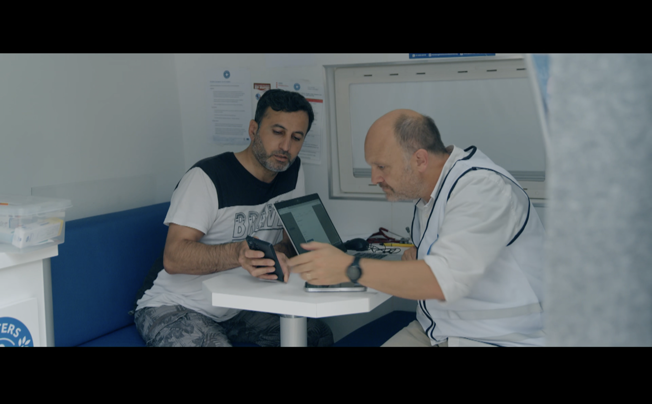 Twee mannen in een medisch kantoor, één van hen een arts met een stethoscoop, die samen naar een tablet kijken.