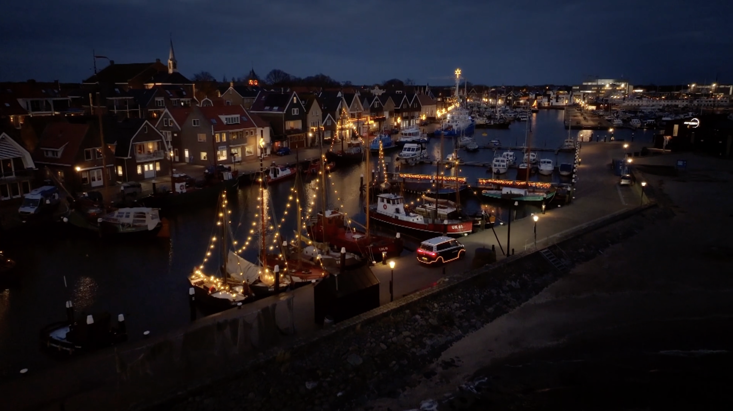 Een rustige havenstad 's avonds met verlichte huizen, boten met lichtjes en een donkere sky.