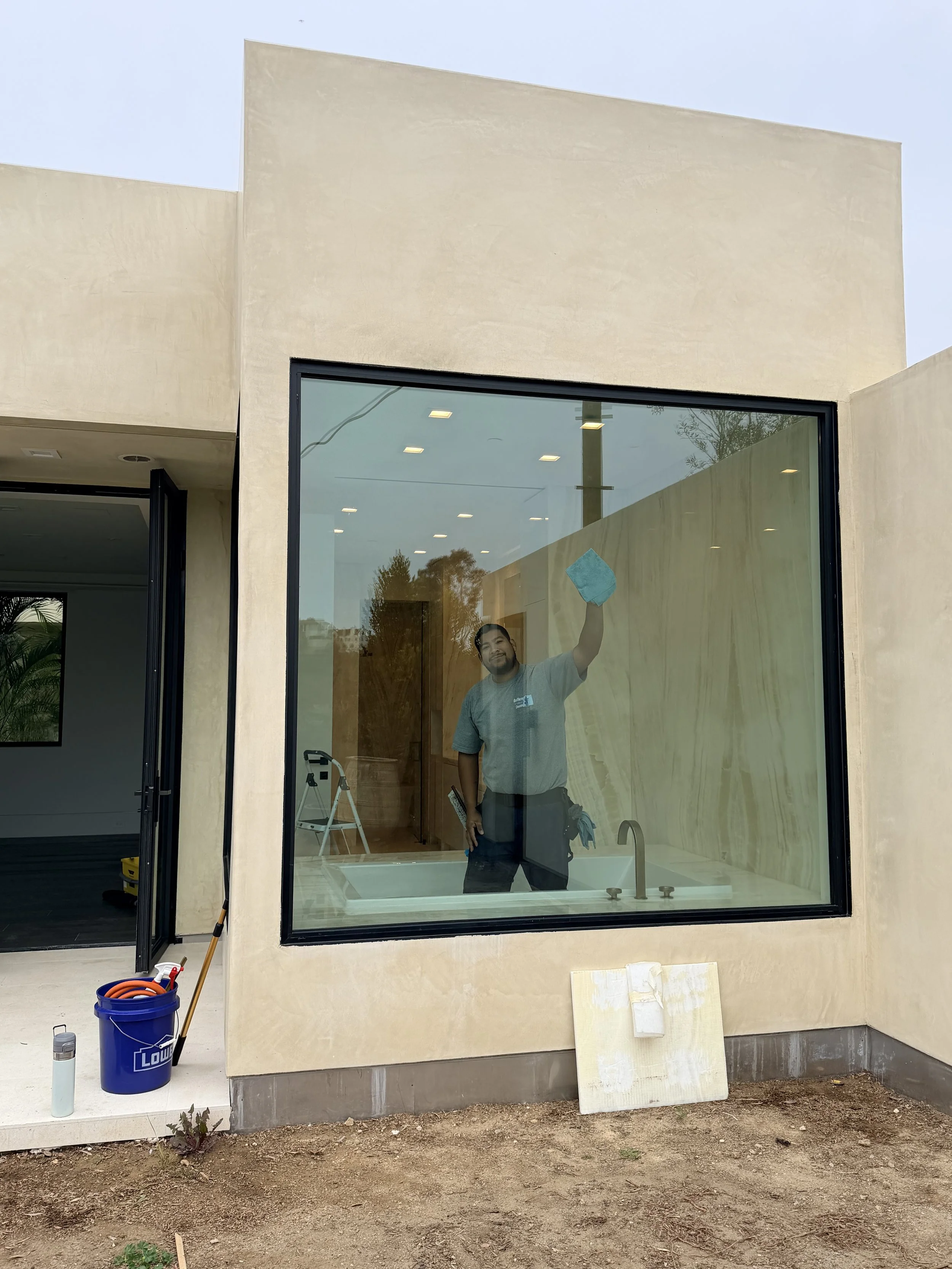Construction worker cleaning a large window of a modern house, with construction tools and materials nearby.