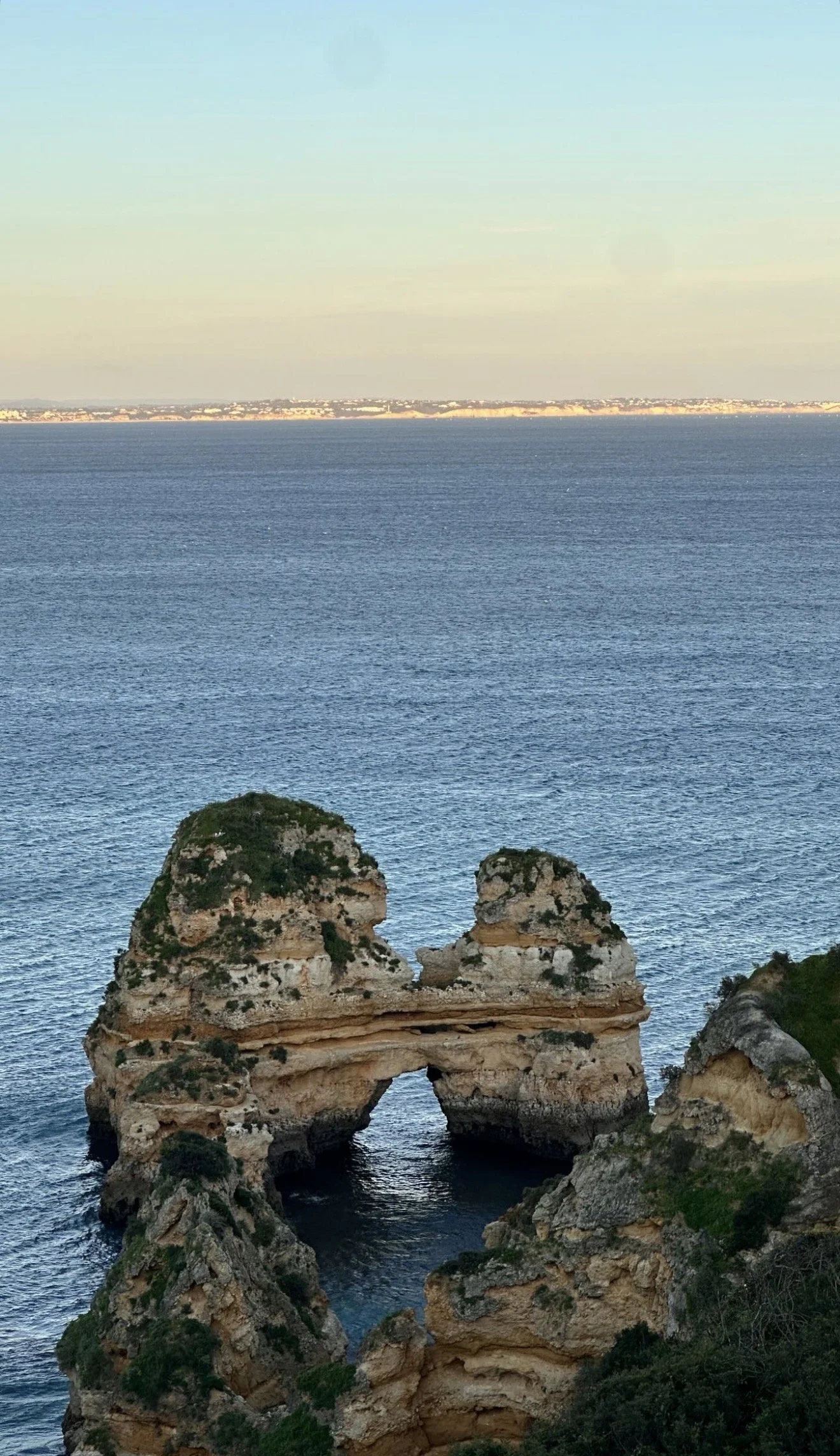 Formação rochosa na esperança, com um arco de pedra na costa, mar azul ao fundo e céu claro.