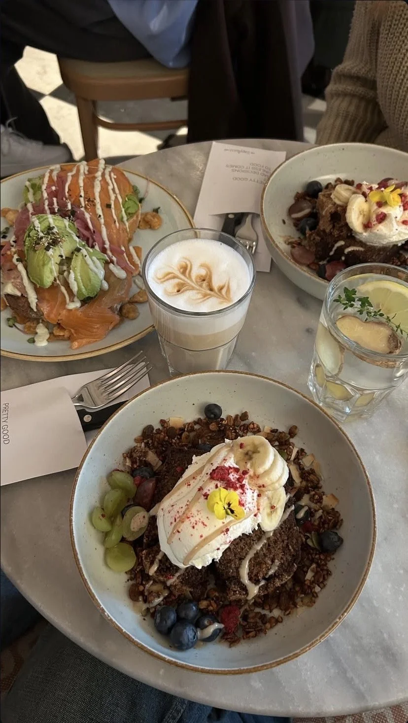 Prato de sobremesas com frutas, sorvete, bolo, uma bebida de leite com caramelo, e uma água com limão, tudo em um ambiente de restaurante.