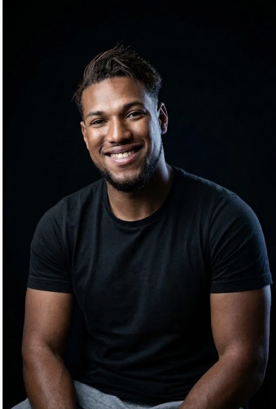 Homem sorrindo, de camiseta preta, com fundo escuro.
