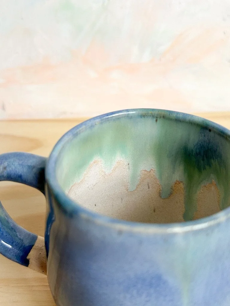 Close-up of a ceramic mug with a blue exterior and a green and cream interior, placed on a wooden surface.