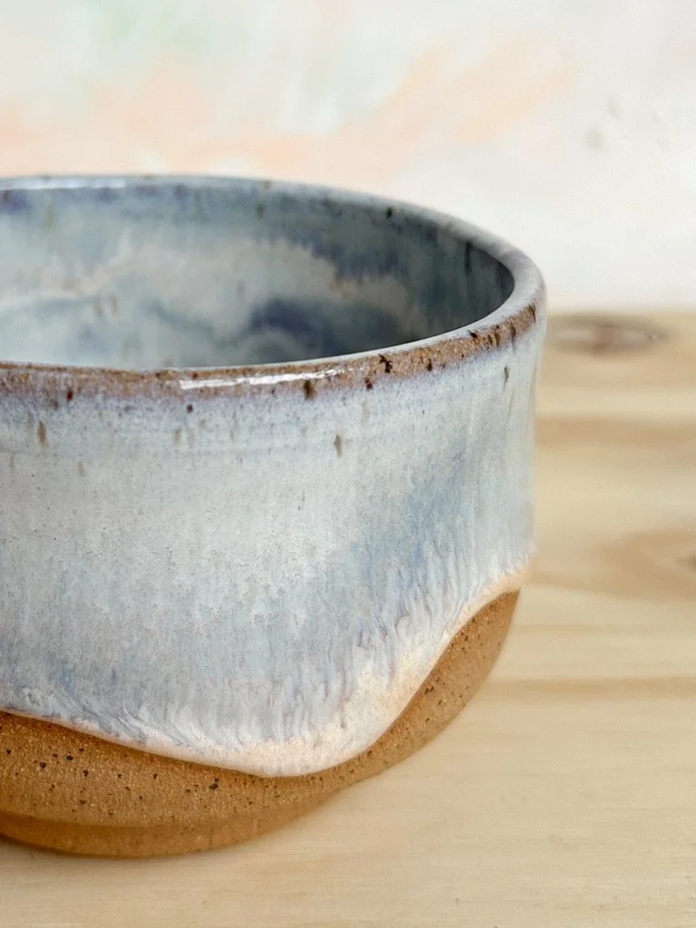 Close-up of a ceramic bowl with a glazed blue and white top and a textured brown bottom, placed on a wooden surface.