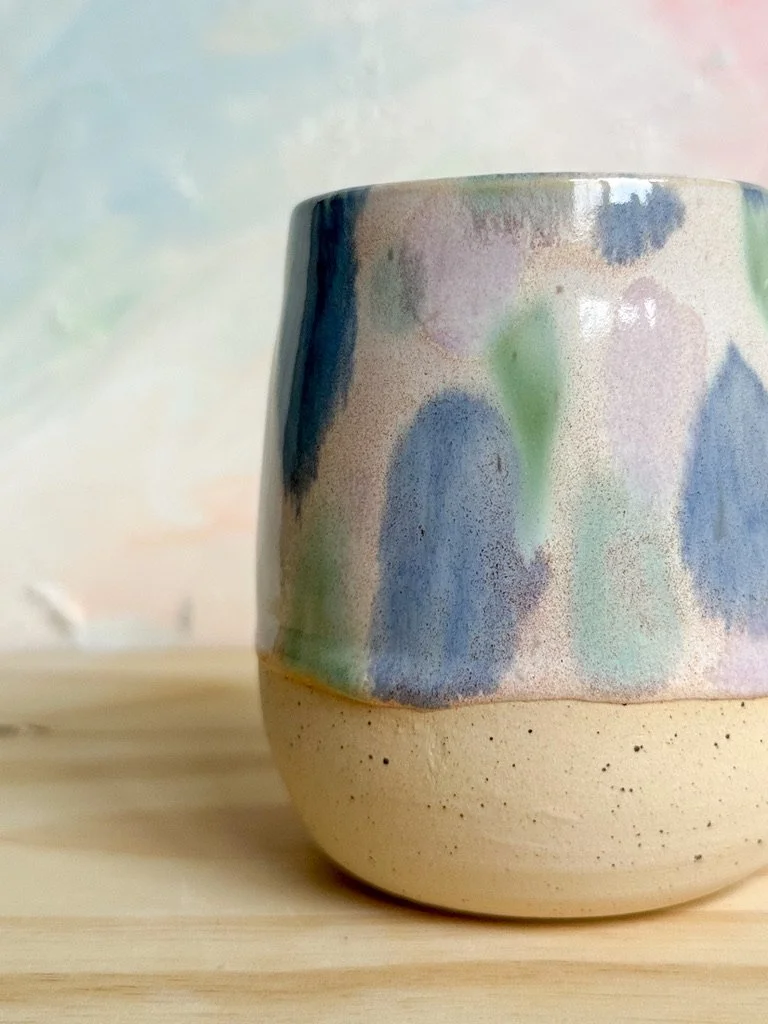 Close-up of a pottery mug with a colorful abstract glaze design on a light wooden surface.