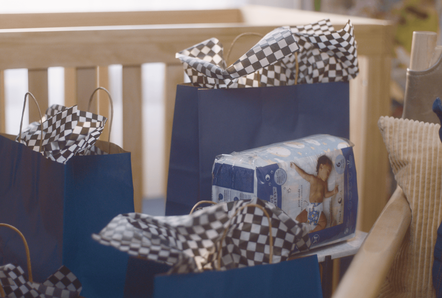 Blue gift bags with black and white checkered tissue paper and a package of baby diapers on a table.