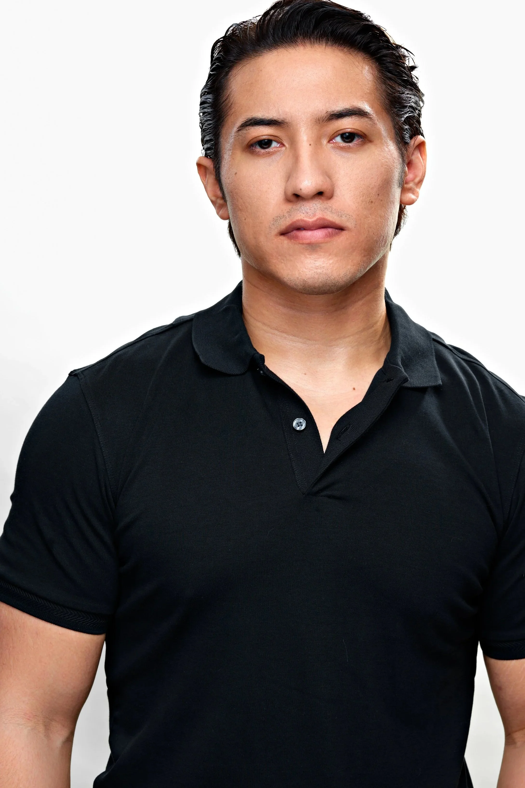 A young man with dark, slicked-back hair, wearing a black short-sleeved polo shirt, looking directly at the camera against a white background.